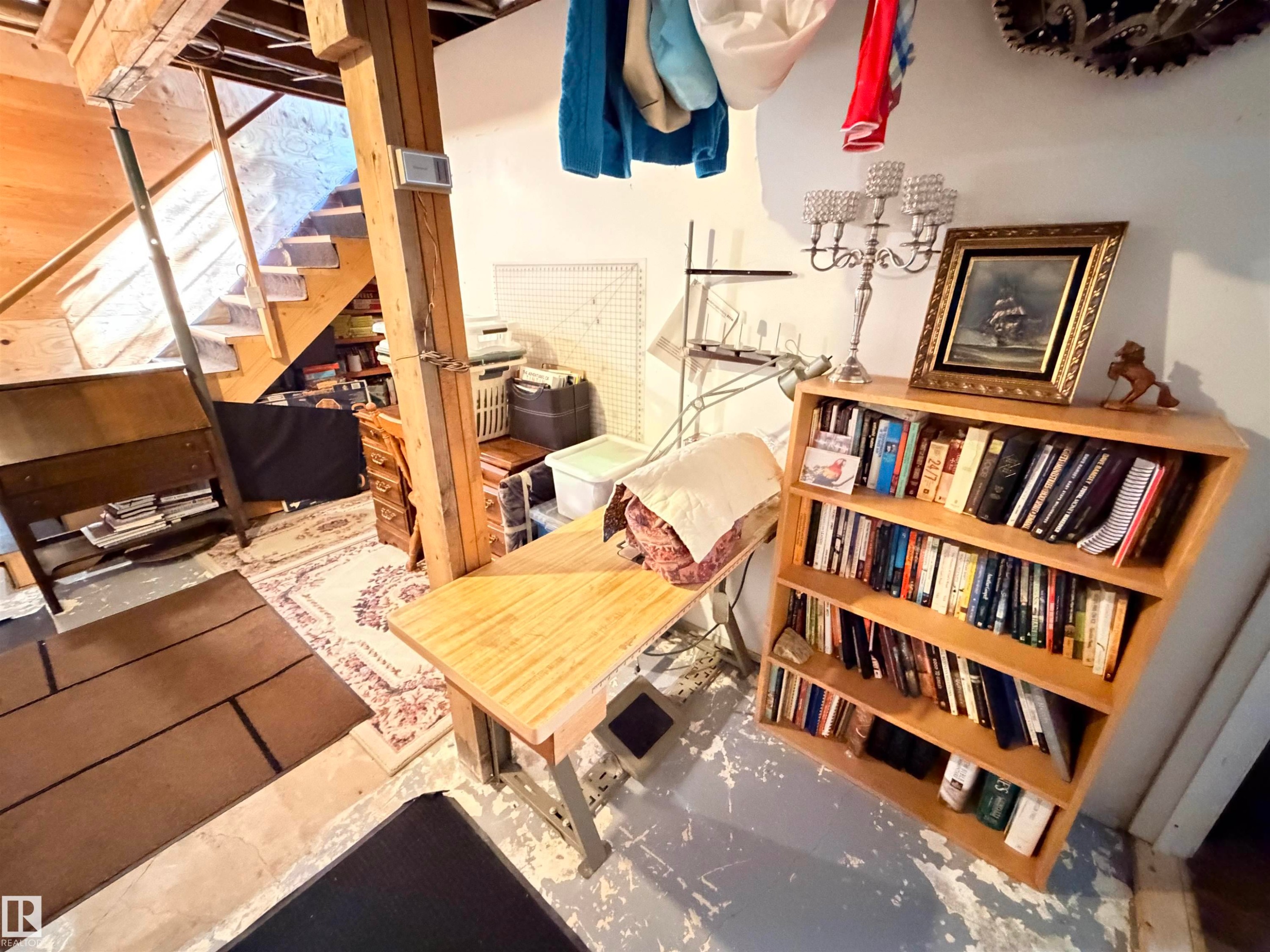 Exposed structural beams and a wooden staircase define this versatile basement area, featuring a light wood-finish bookshelf and a work table - 4823 49 Street, Clyde, AB - Indoor Photo Showing Other Room