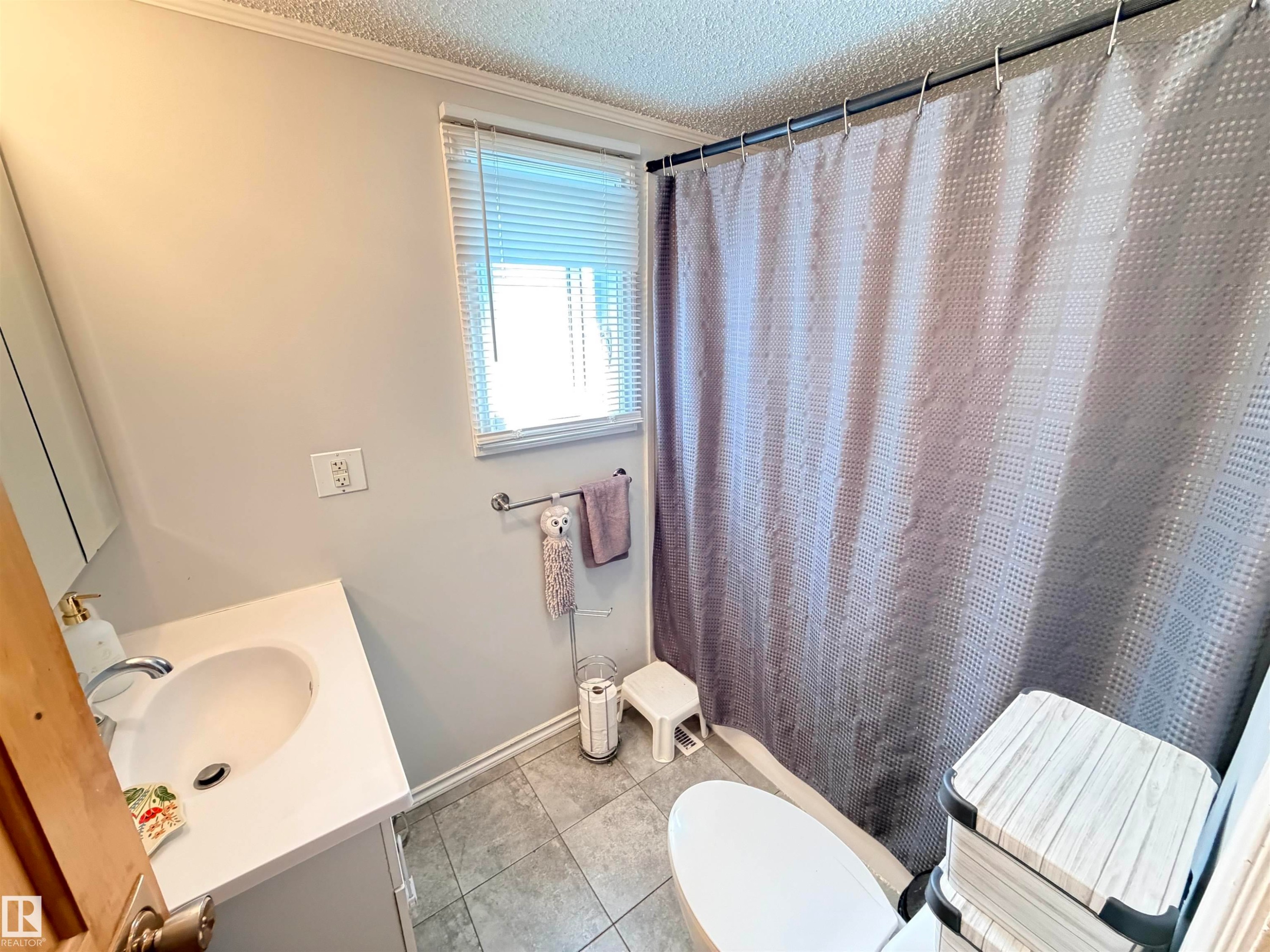 Bathroom featuring a single window with blinds, a white vanity with an integrated sink, a chrome faucet, and tiled flooring - 4823 49 Street, Clyde, AB - Indoor Photo Showing Bathroom