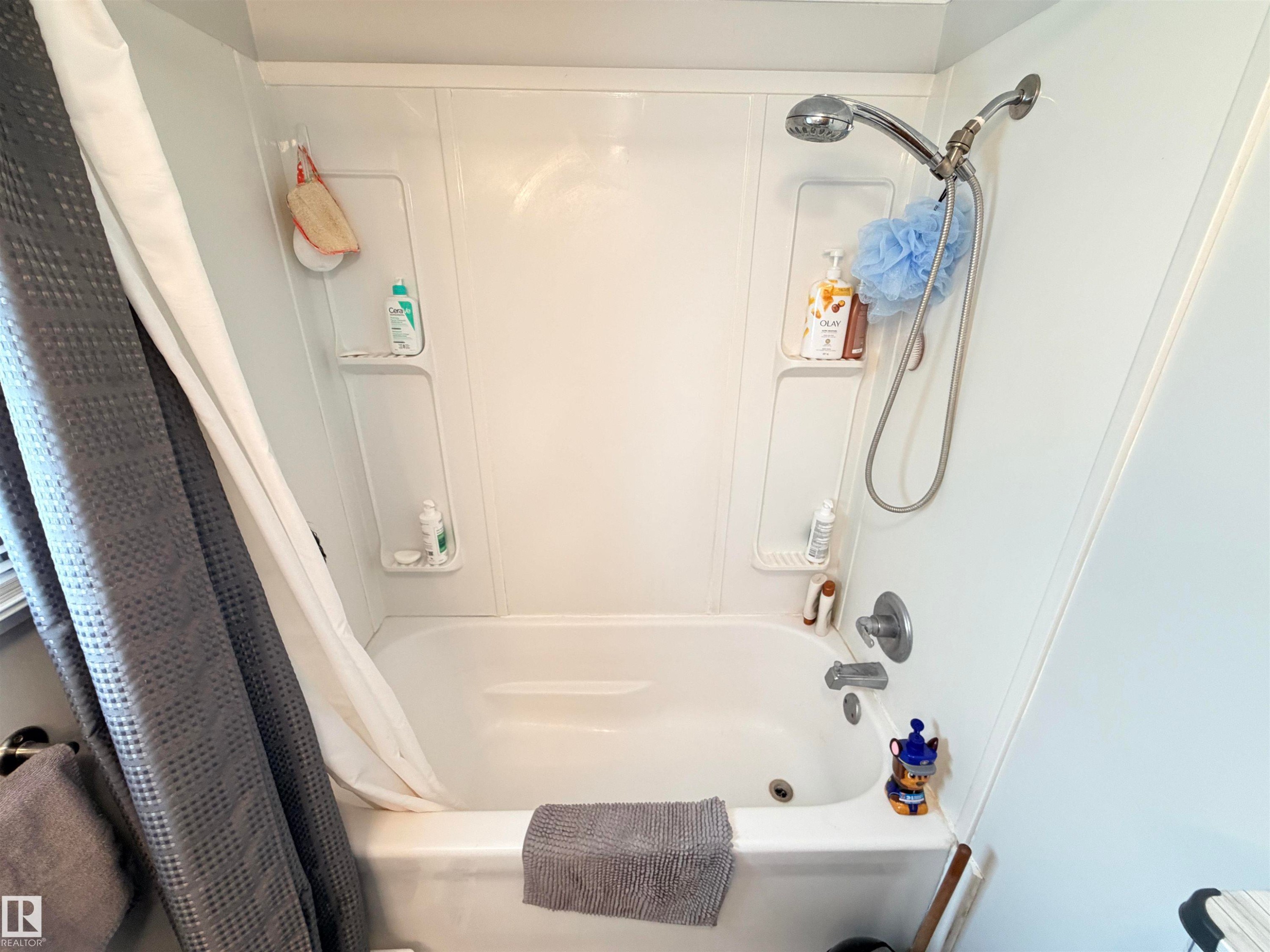 White bathtub with integrated wall-mounted shelving and a chrome showerhead with hose attachment - 4823 49 Street, Clyde, AB - Indoor Photo Showing Bathroom