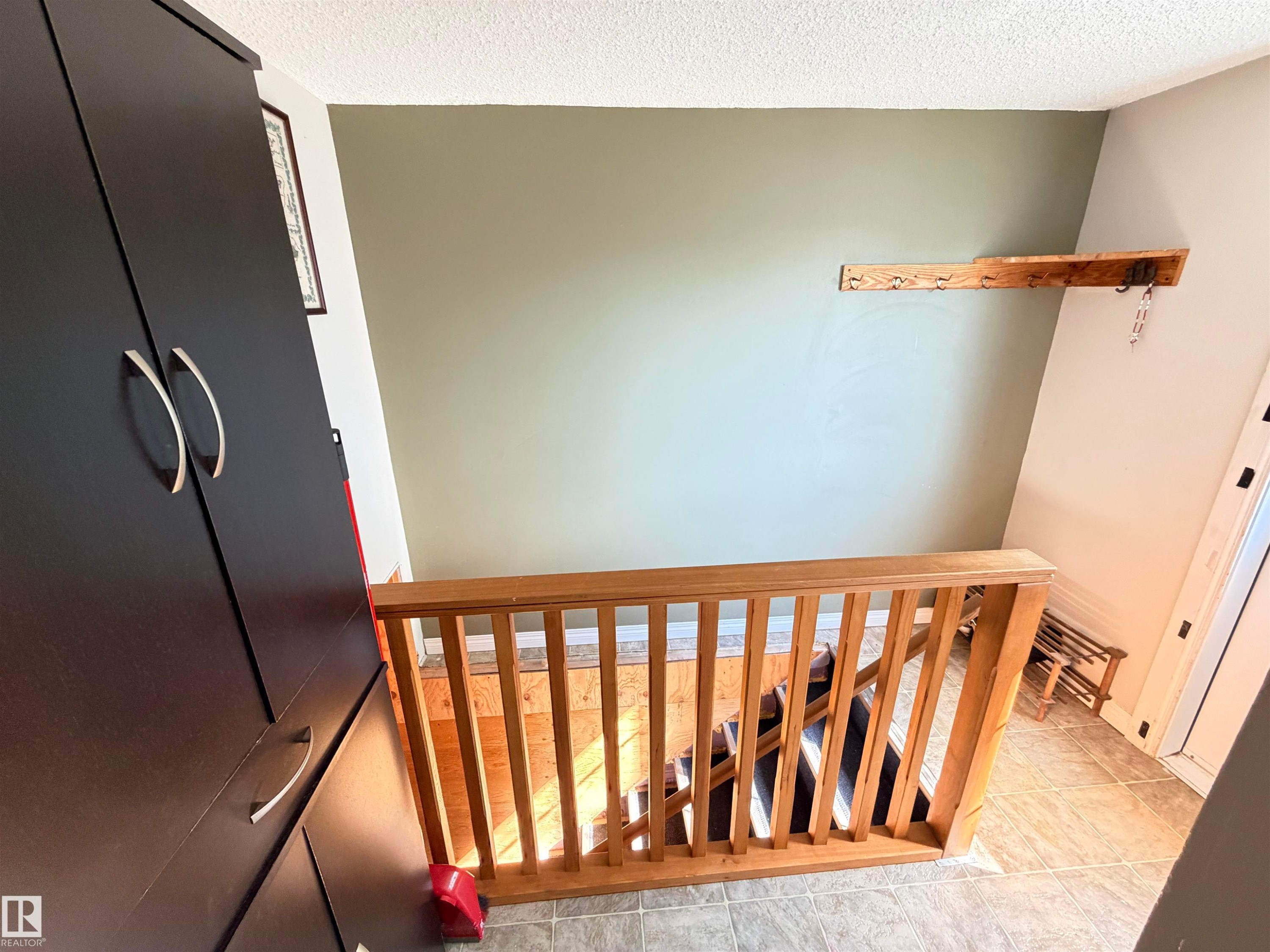 Wood-finish staircase railing with vertical balusters - 4823 49 Street, Clyde, AB - Indoor Photo Showing Other Room