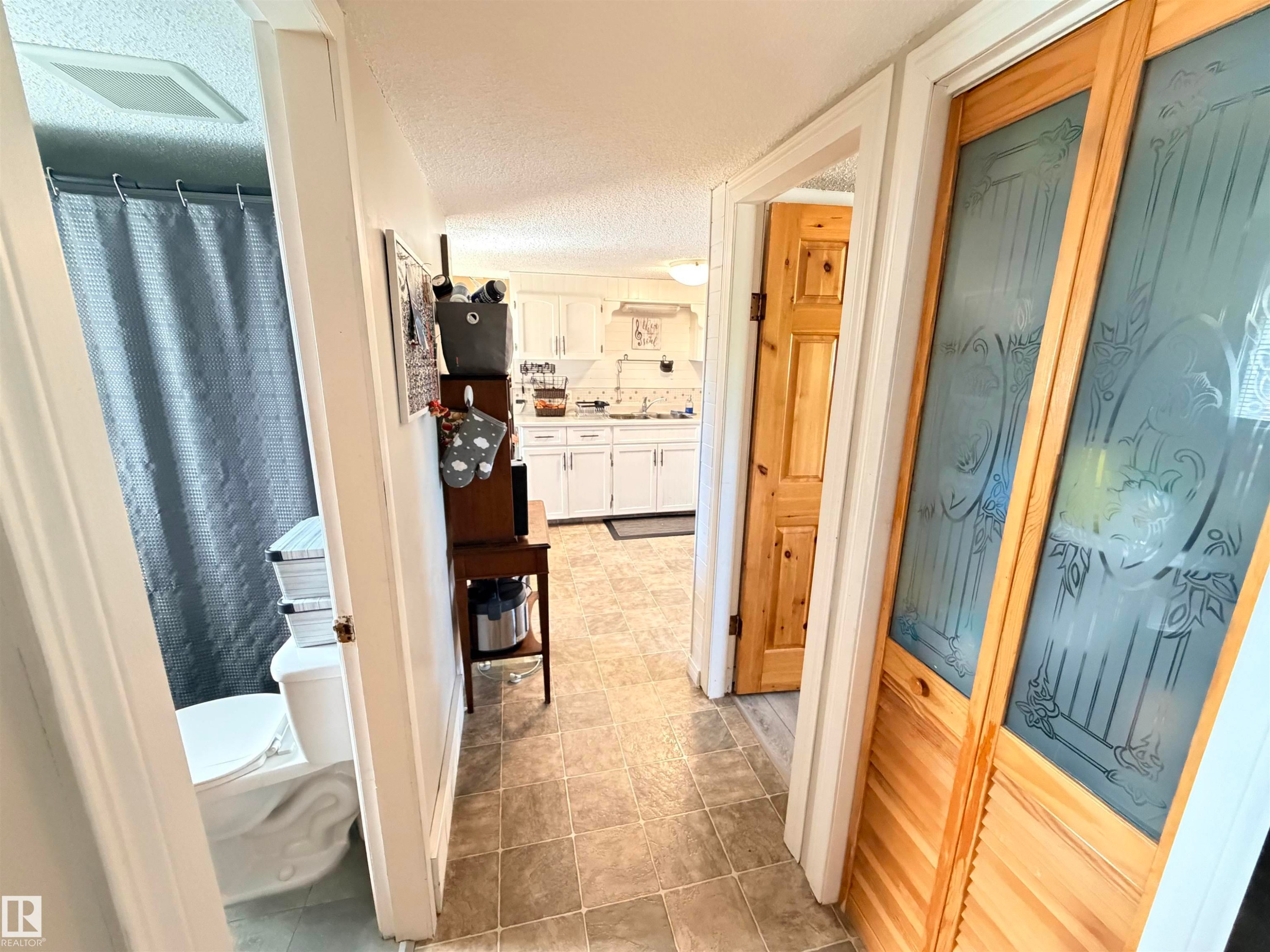 Hallway with tile flooring, featuring a bathroom entrance, a wood panel door, and decorative frosted glass bifold doors - 4823 49 Street, Clyde, AB - Indoor Photo Showing Bathroom