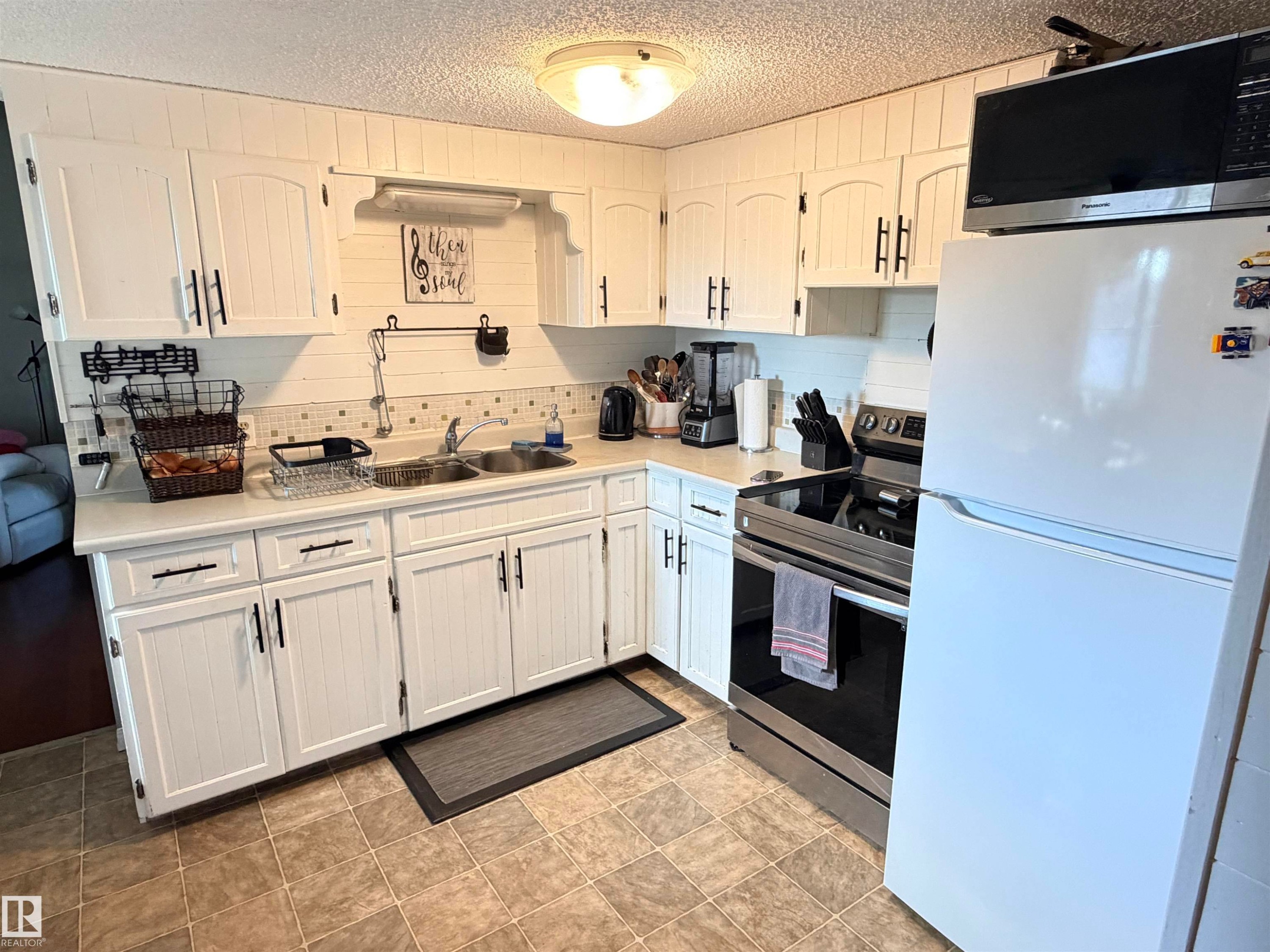 Kitchen featuring white panel cabinetry with black hardware, a stainless steel electric range, and a double basin sink - 4823 49 Street, Clyde, AB - Indoor Photo Showing Kitchen