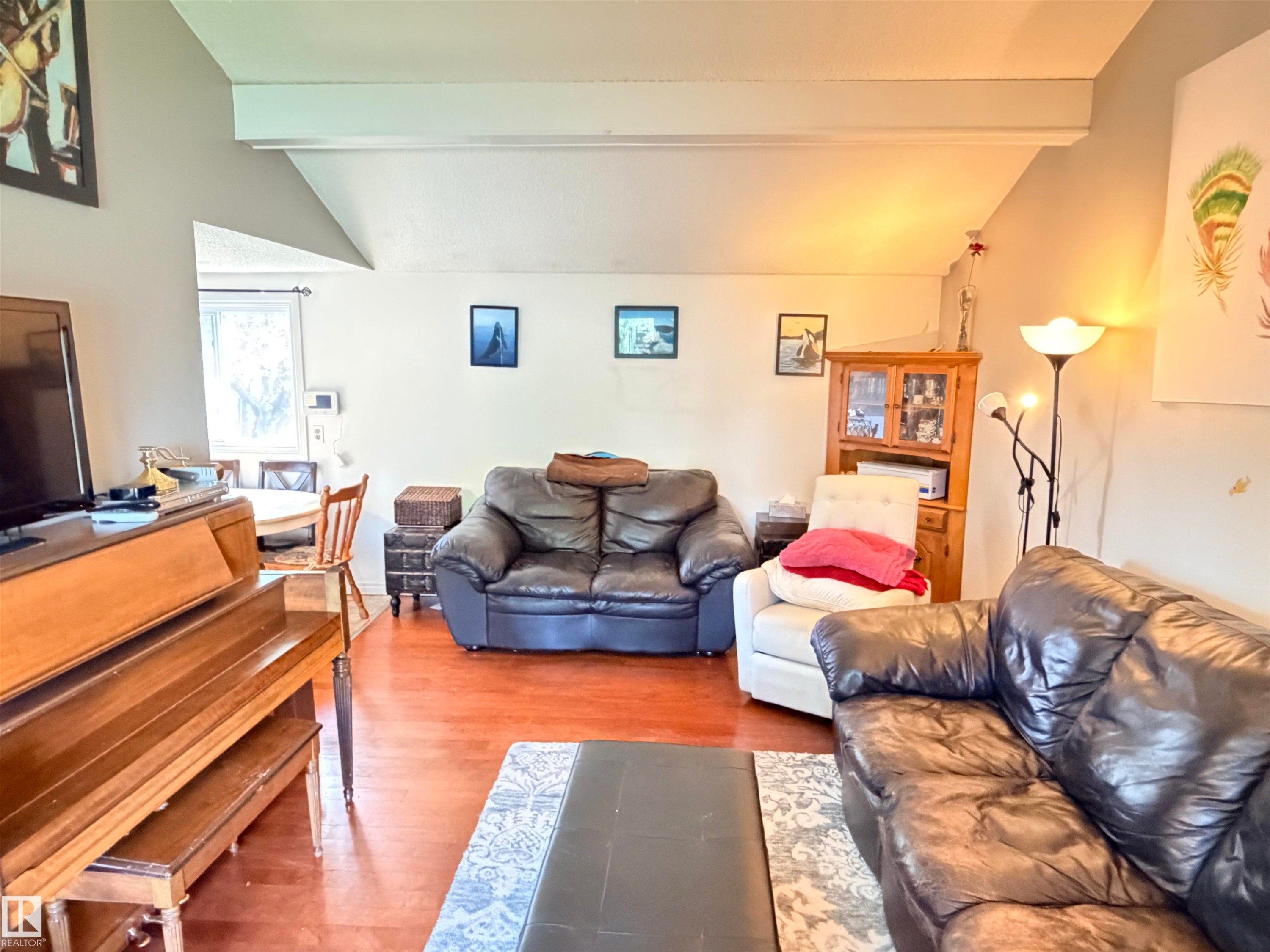 Open-concept living area featuring wood-finish flooring, a vaulted ceiling with exposed beams, and a dining area with natural light - 4823 49 Street, Clyde, AB - Indoor Photo Showing Living Room