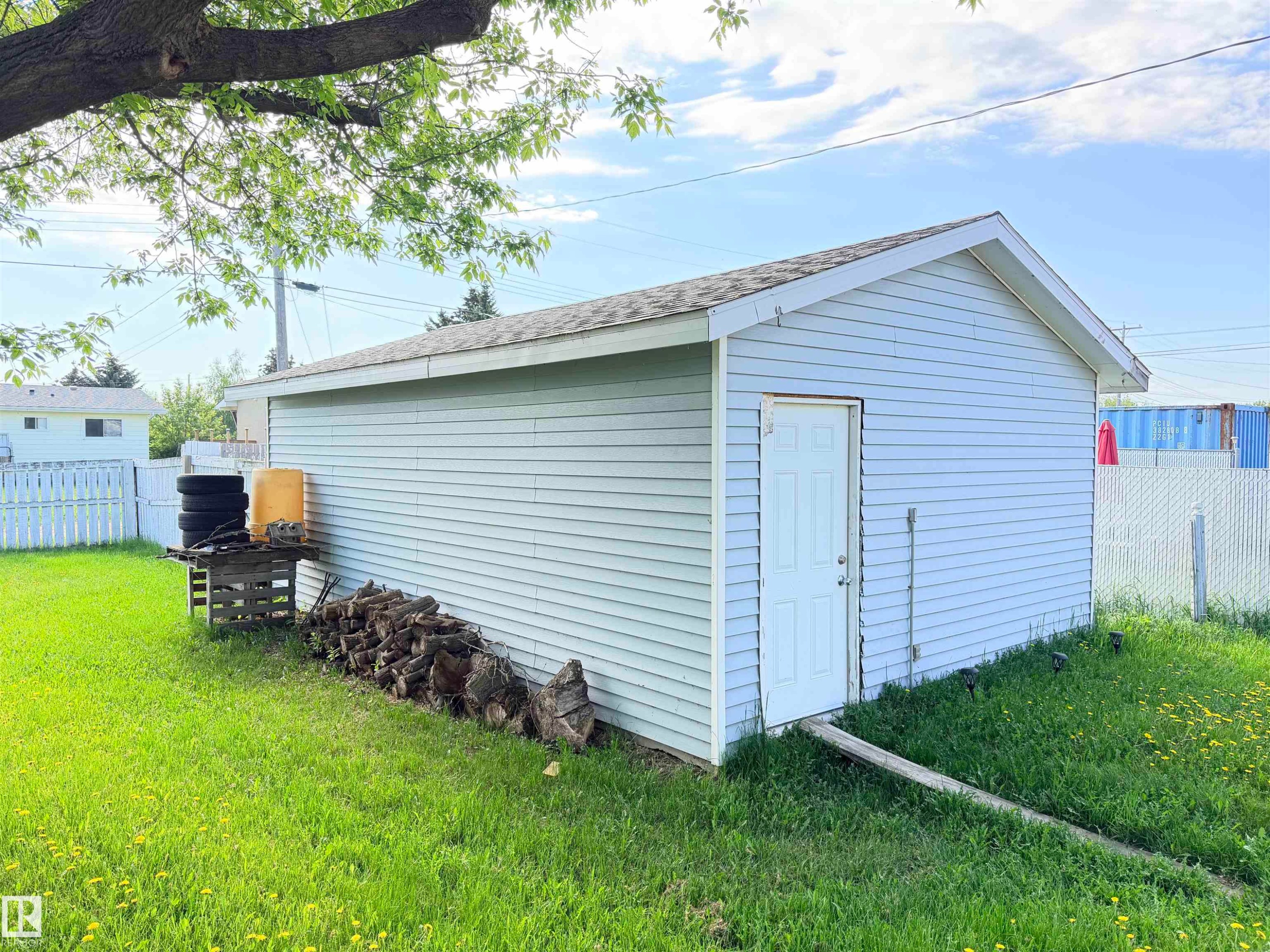 Detached outbuilding with light blue siding and a white paneled door, featuring a pitched roof and a green grassy area - 4823 49 Street, Clyde, AB - Outdoor
