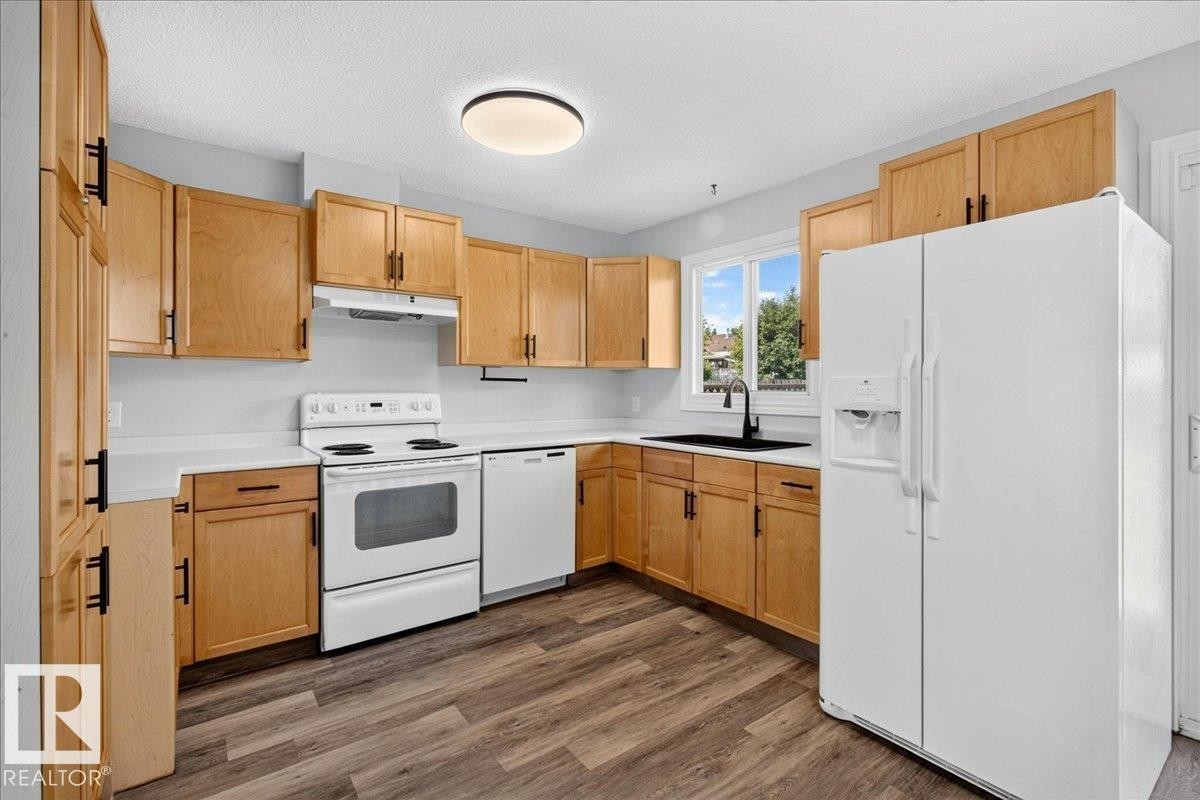 Kitchen featuring wood-finish cabinetry, white countertops, a white appliance suite, a black basin sink with a matte black faucet, and wood-finish flooring - 4212 32 Avenue Nw, Edmonton, AB - Indoor Photo Showing Kitchen