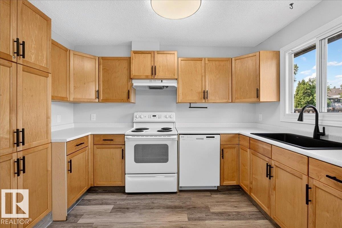 U-shaped kitchen featuring light wood-finish cabinetry with black hardware, white countertops, and wood-finish flooring - 4212 32 Avenue Nw, Edmonton, AB - Indoor Photo Showing Kitchen