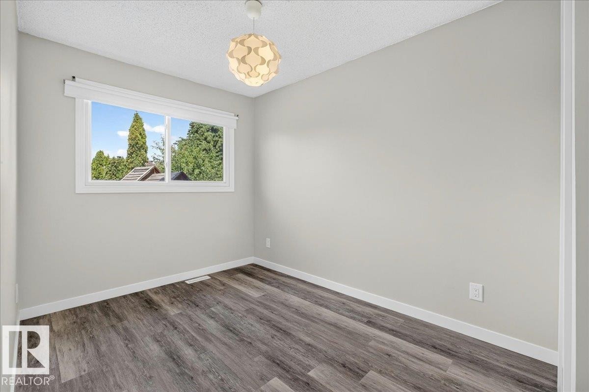 Neutral-toned room featuring a large window, contemporary ceiling light fixture, wood-finish flooring, and white baseboards - 4212 32 Avenue Nw, Edmonton, AB - Indoor Photo Showing Other Room