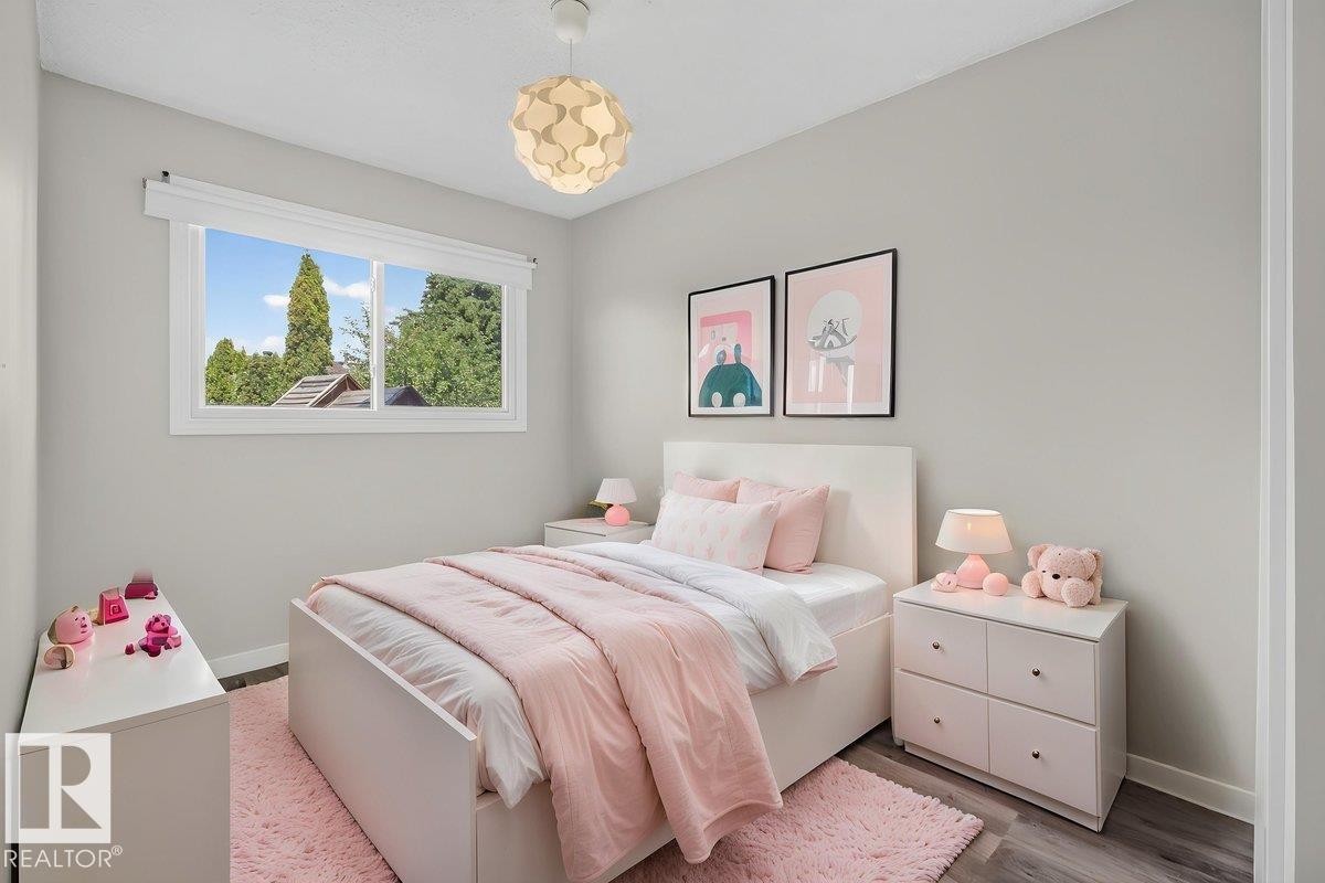Bedroom featuring light gray walls, wood-finish flooring, a white window frame with a roller blind, and a contemporary ceiling light fixture - 4212 32 Avenue Nw, Edmonton, AB - Indoor Photo Showing Bedroom