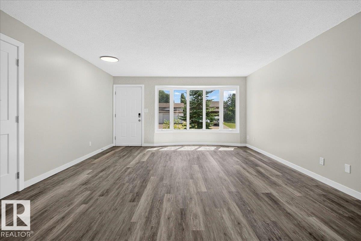 Spacious interior room featuring wood-finish flooring, light gray wall paint, and white baseboards - 4212 32 Avenue Nw, Edmonton, AB - Indoor