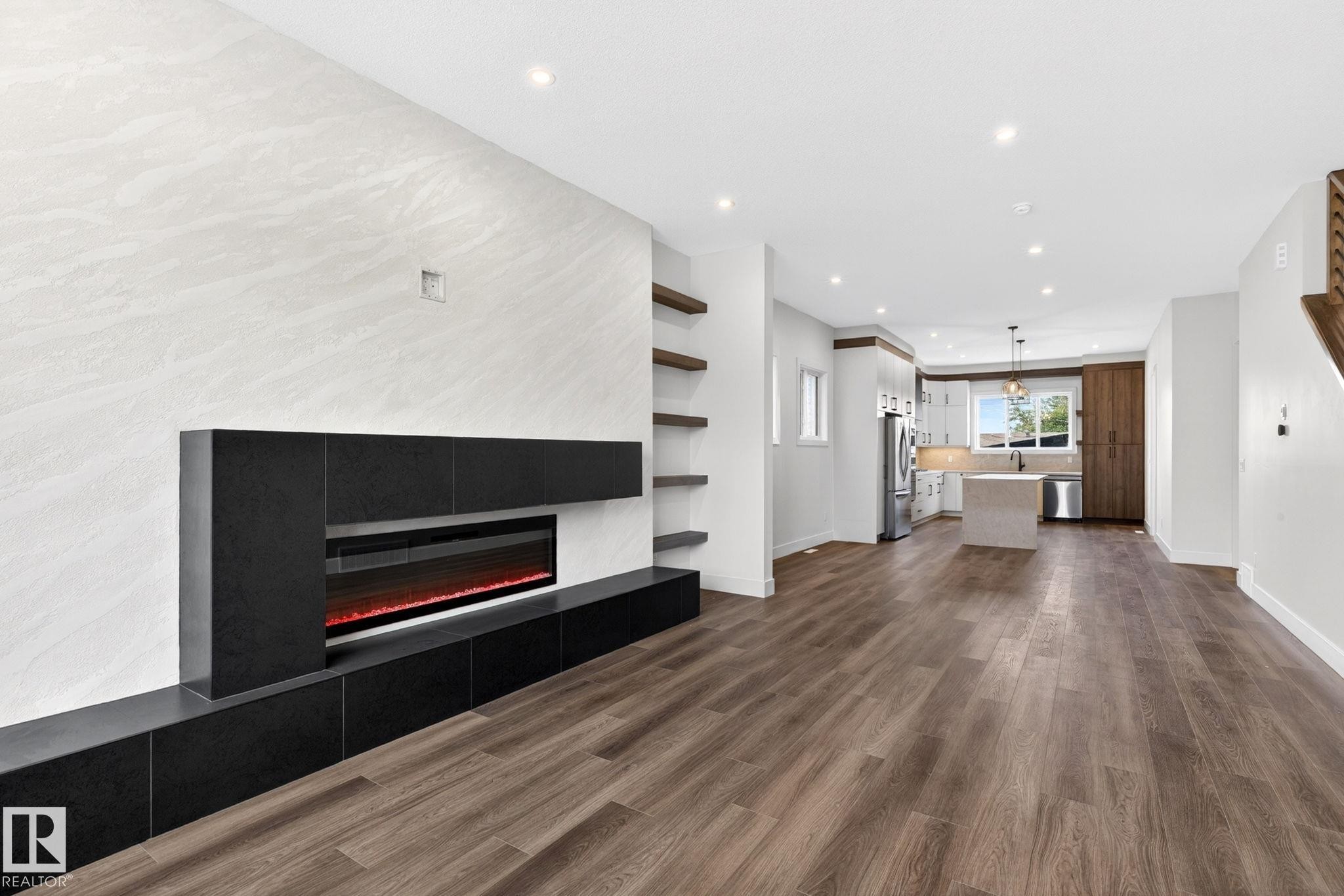 Spacious living area featuring a linear electric fireplace with black built-in cabinetry, wood-finish flooring, recessed lighting, and open shelving - 5308 103A Avenue, Edmonton, AB - Indoor With Fireplace