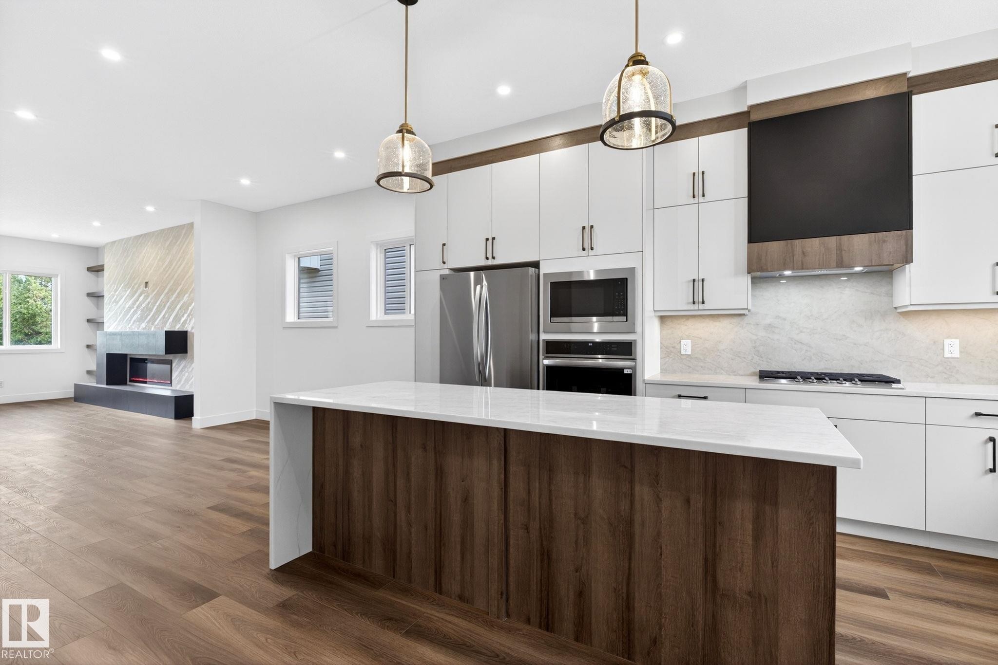 Contemporary kitchen featuring white cabinetry, stainless steel appliances, a center island with a light-toned countertop, and wood-finish flooring - 5308 103A Avenue, Edmonton, AB - Indoor Photo Showing Kitchen With Upgraded Kitchen