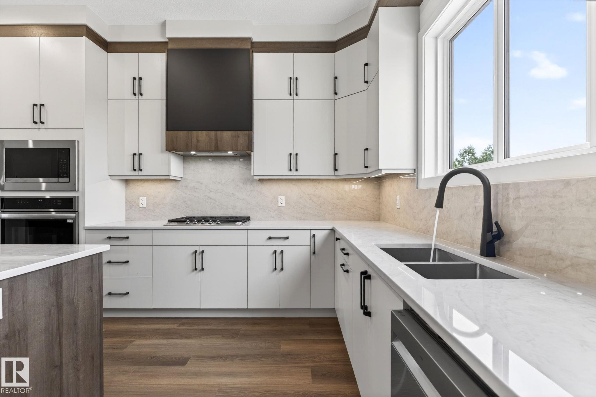 Contemporary kitchen featuring white cabinetry with dark hardware, light-toned stone backsplash, and wood-finish flooring - 5308 103A Avenue, Edmonton, AB - Indoor Photo Showing Kitchen With Double Sink With Upgraded Kitchen
