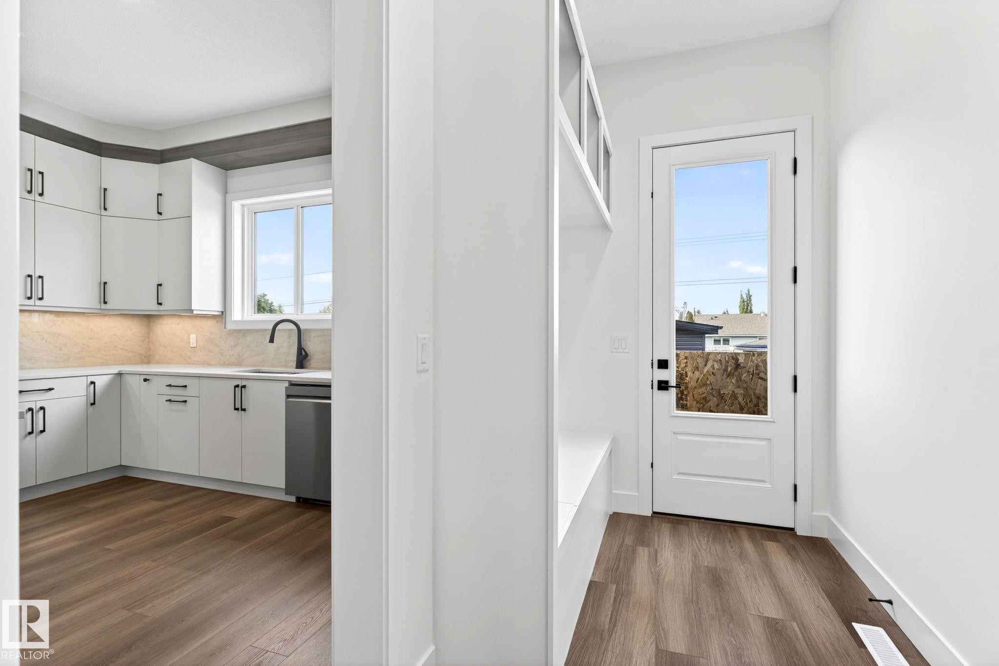 Open concept kitchen featuring white cabinetry, under-cabinet lighting, a corner sink with a black faucet, and a stainless steel dishwasher - 5308 103A Avenue, Edmonton, AB - Indoor Photo Showing Kitchen