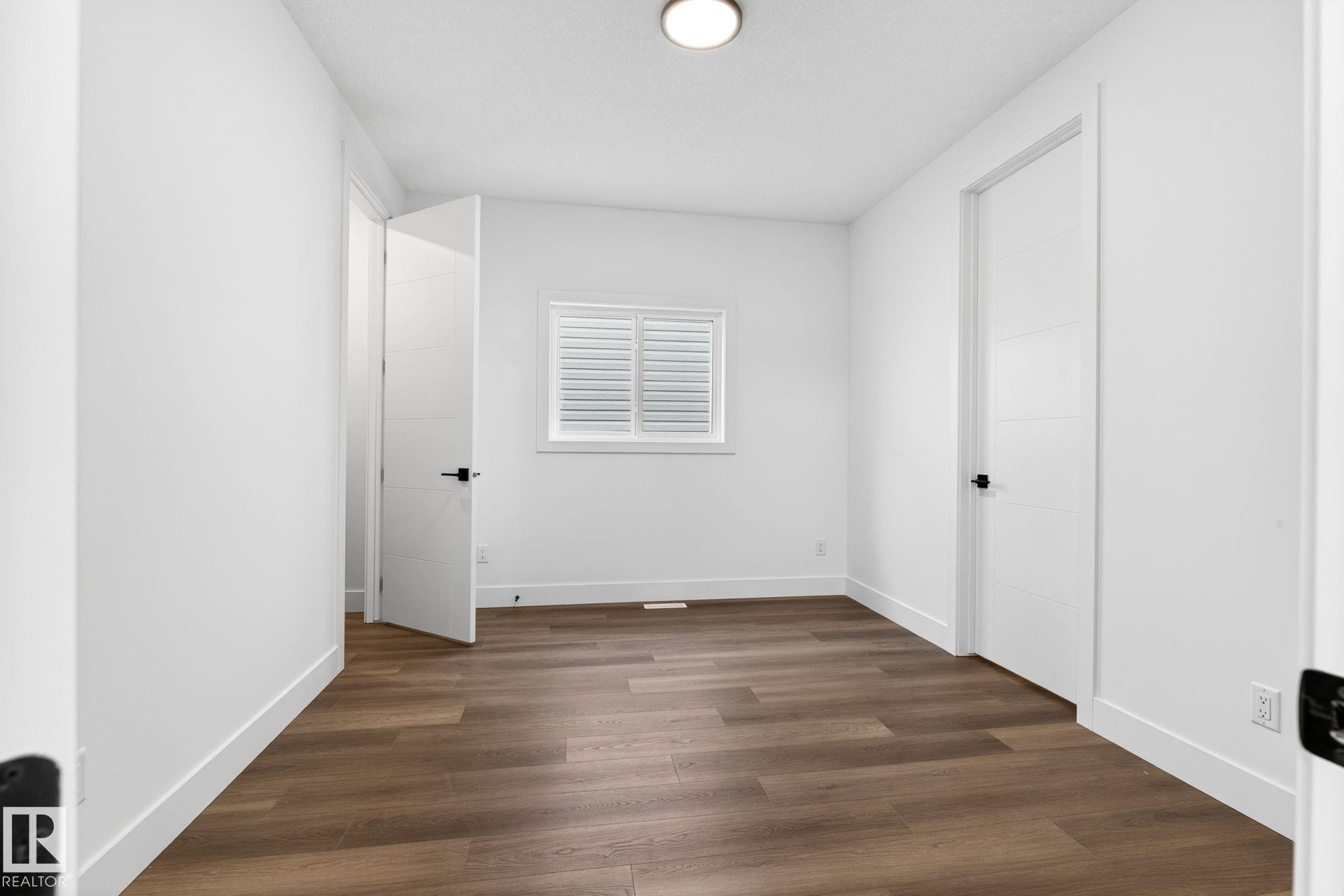 Room featuring wood-finish flooring, white baseboards, and bright white walls - 5308 103A Avenue, Edmonton, AB - Indoor Photo Showing Other Room