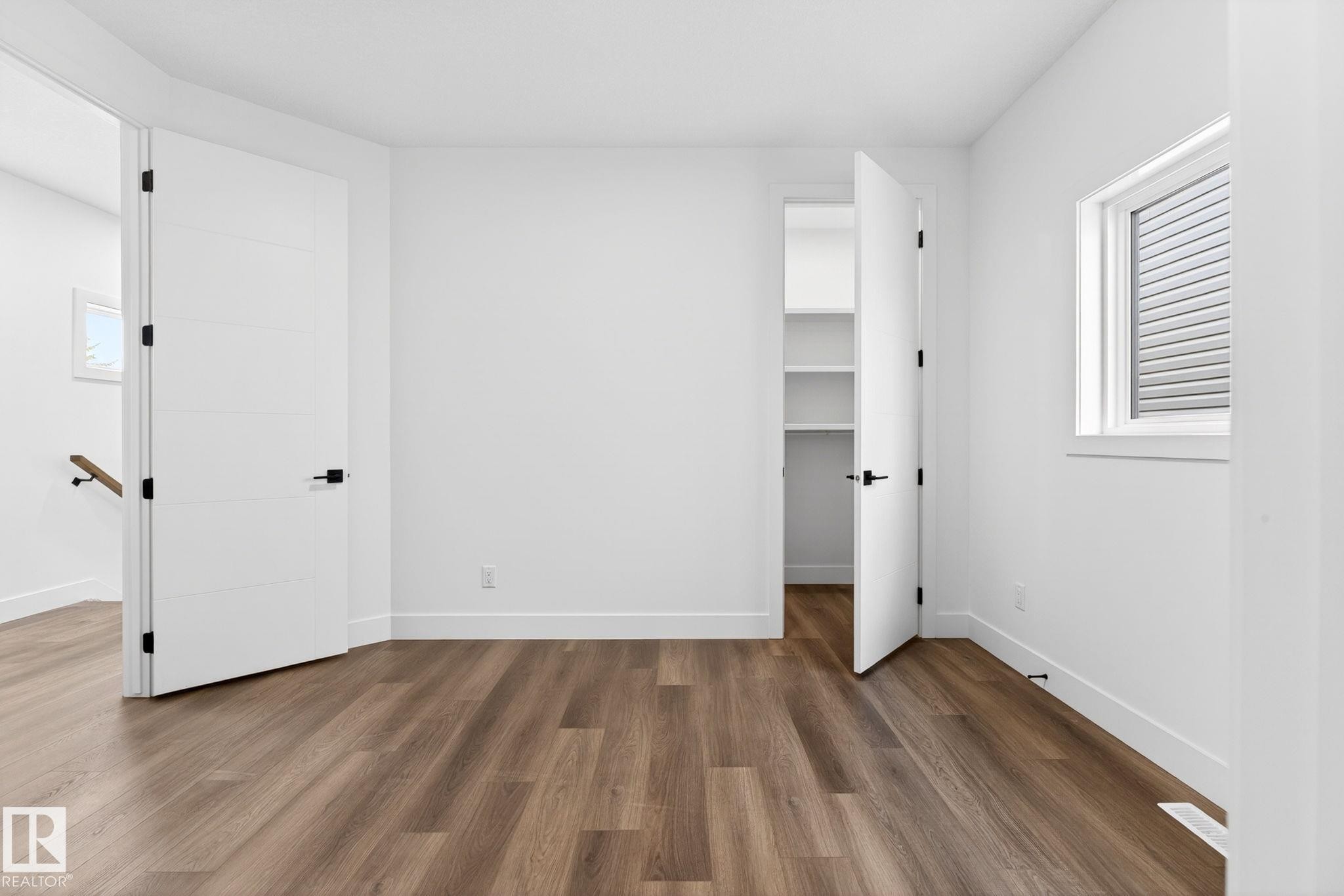 Bright room featuring wood-finish flooring, white walls, and a window with horizontal blinds - 5308 103A Avenue, Edmonton, AB - Indoor Photo Showing Other Room