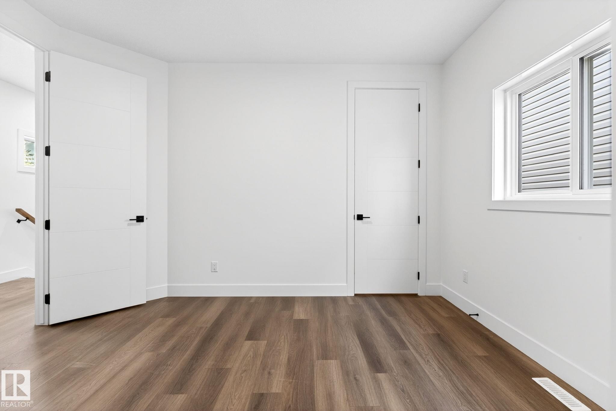 Bright interior space featuring wood-finish flooring, white walls, and a window with horizontal blinds - 5308 103A Avenue, Edmonton, AB - Indoor Photo Showing Other Room