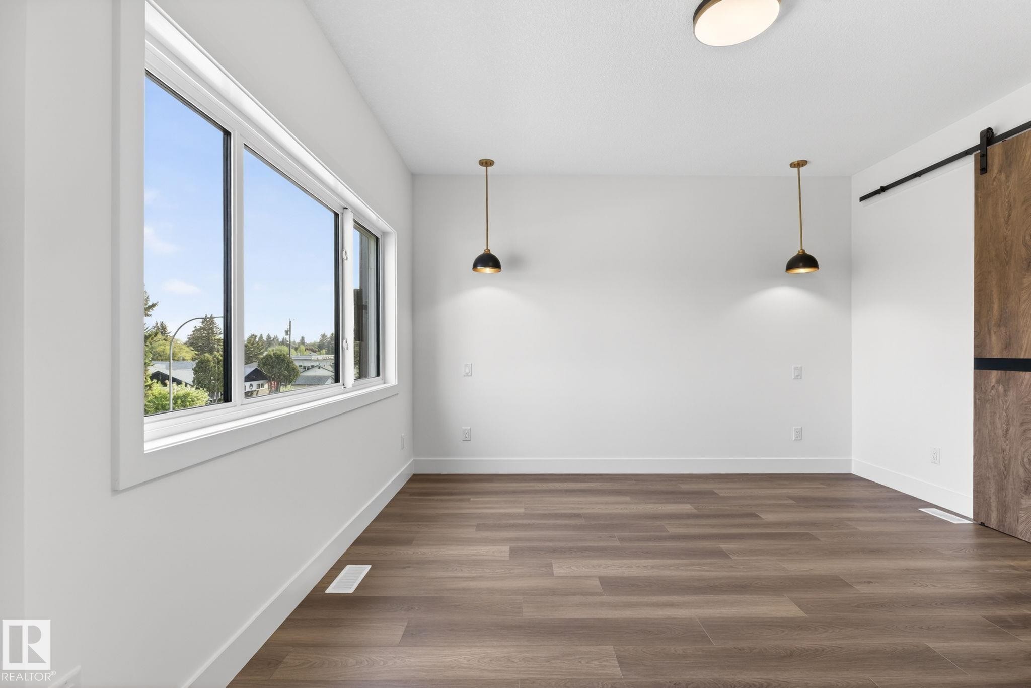 Spacious room featuring wood-finish flooring, white baseboards, and a large multi-pane window - 5308 103A Avenue, Edmonton, AB - Indoor Photo Showing Other Room