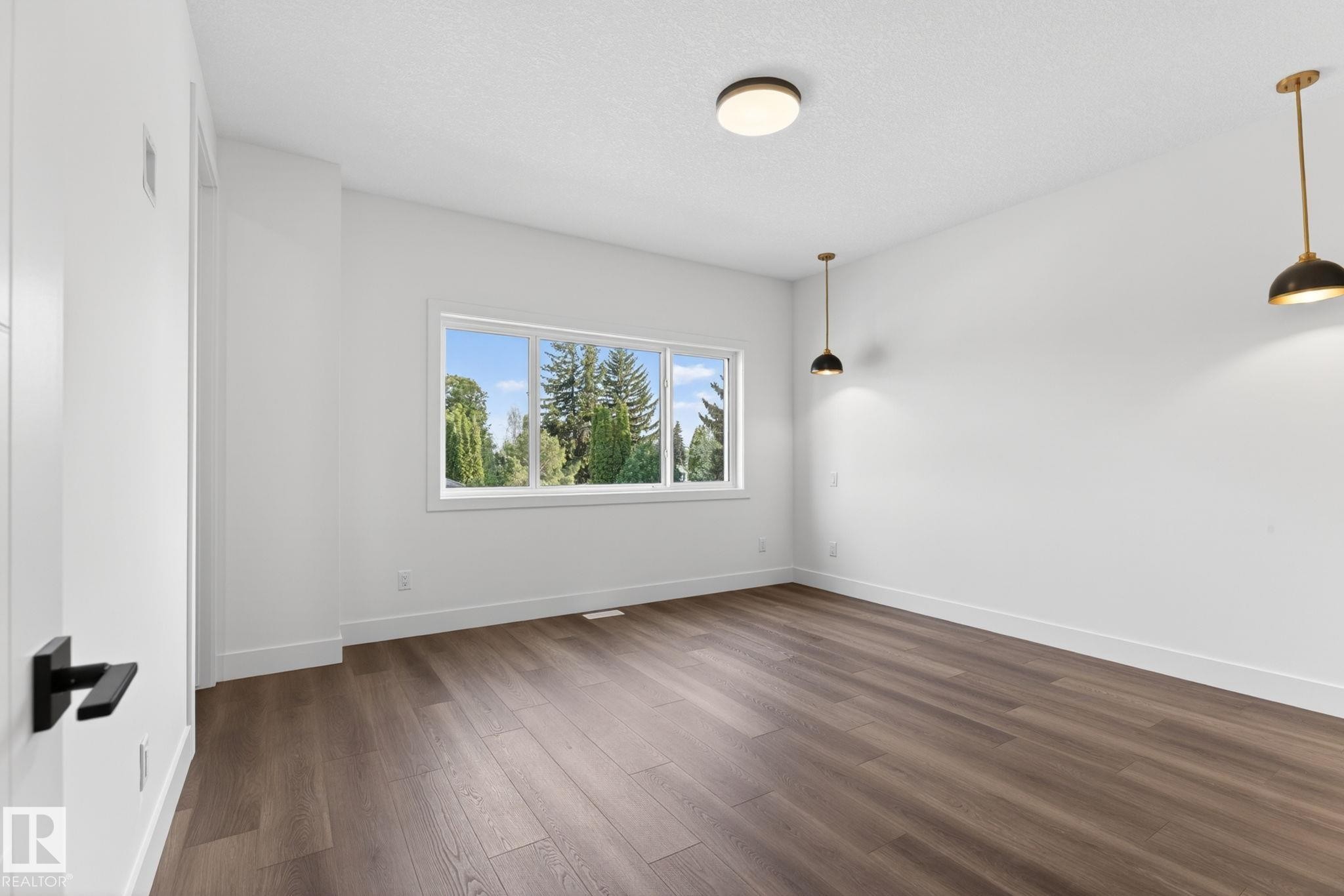 Spacious room featuring wood-finish flooring, white walls, and a large window with exterior tree scenery - 5308 103A Avenue, Edmonton, AB - Indoor Photo Showing Other Room