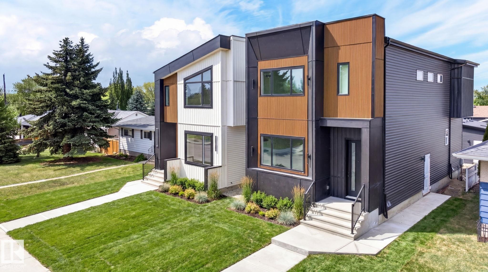 Modern duplex exterior featuring contrasting dark and light siding, wood-look accents, black-framed windows, and a manicured lawn with a concrete pathway - 5308 103A Avenue, Edmonton, AB - Outdoor