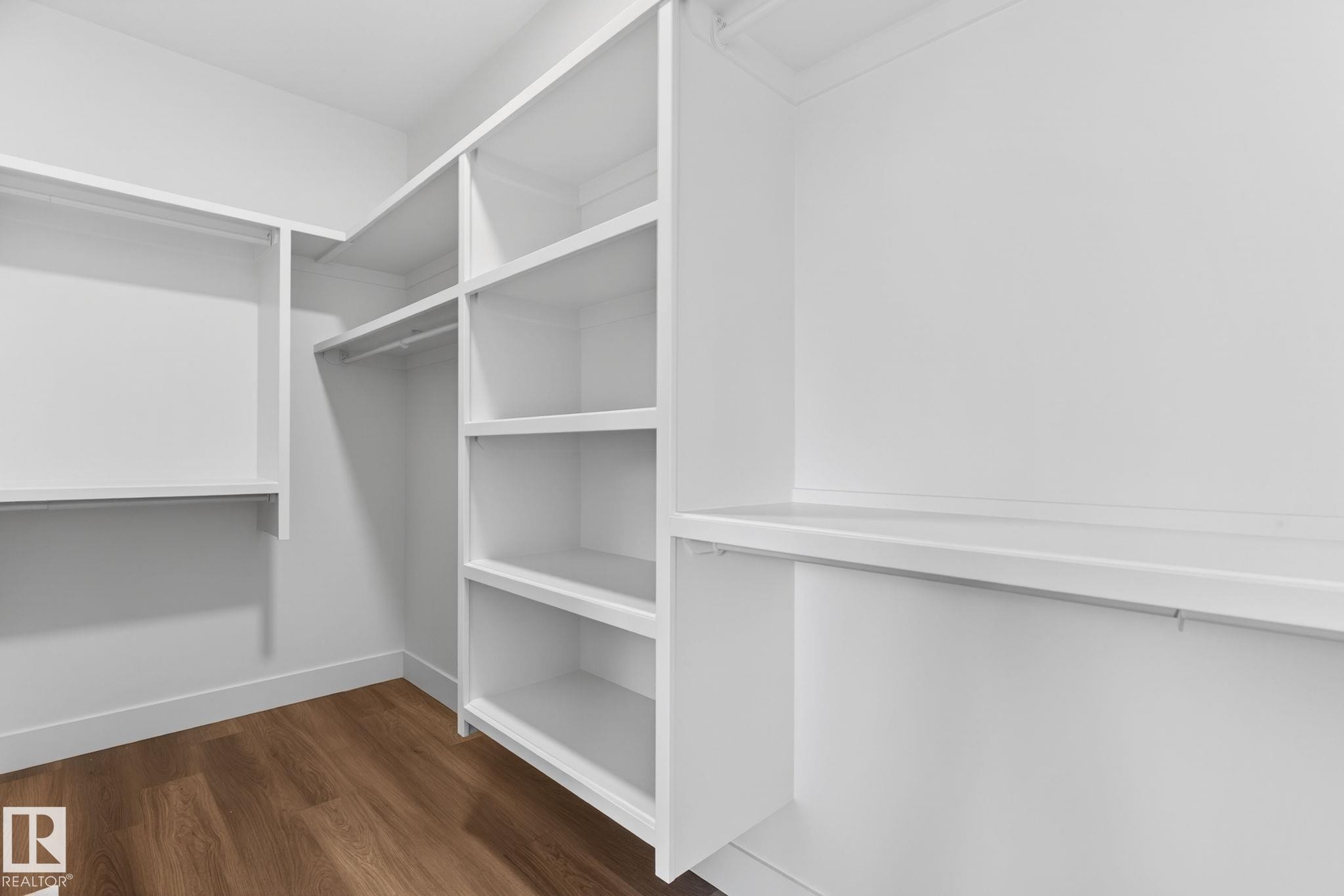 Walk-in closet featuring built-in white shelving, multiple hanging rods, and wood-finish flooring - 5308 103A Avenue, Edmonton, AB - Indoor With Storage