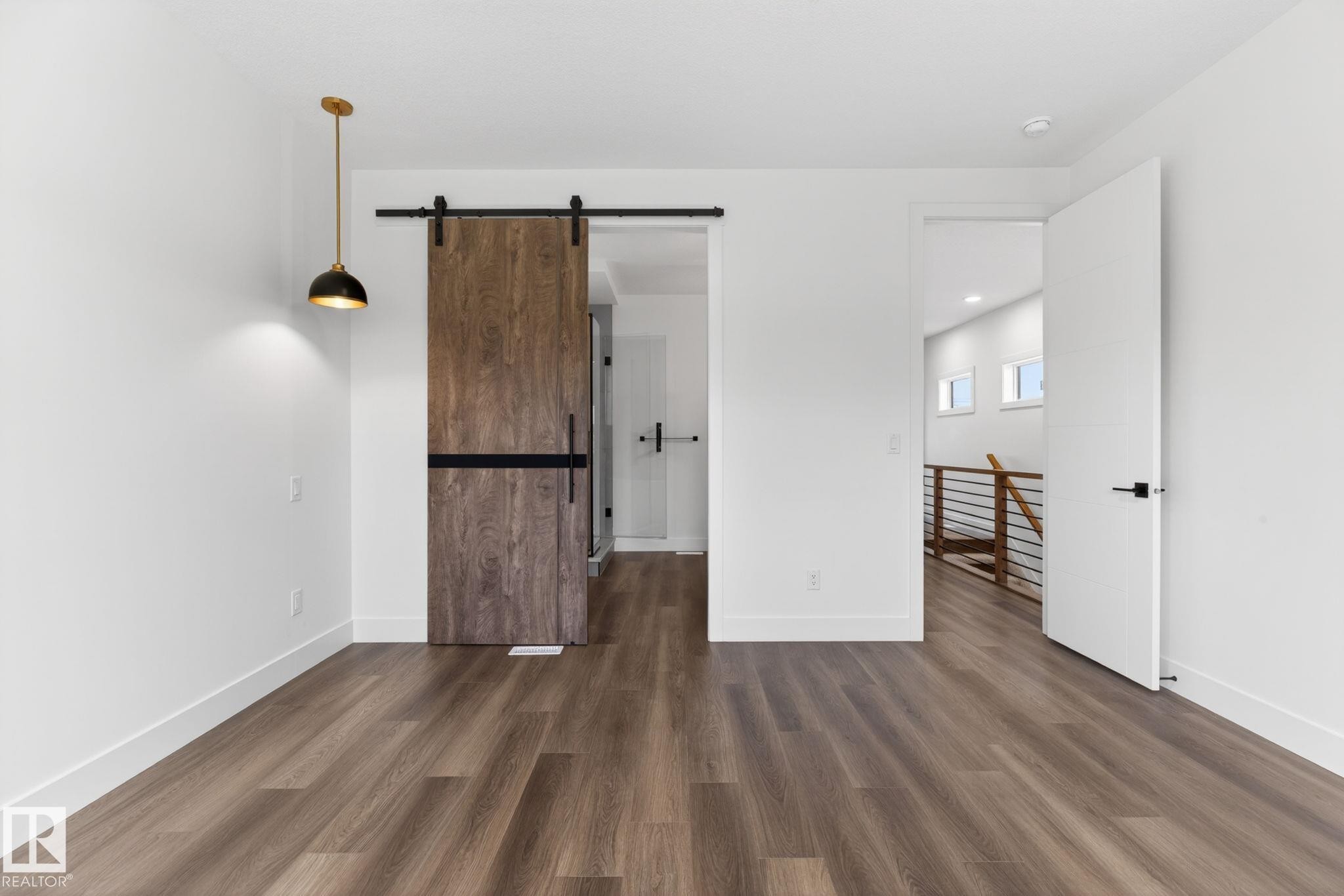 Spacious room featuring wood-finish flooring, a modern barn door with black hardware, a contemporary pendant light fixture, and white trim - 5308 103A Avenue, Edmonton, AB - Indoor Photo Showing Other Room