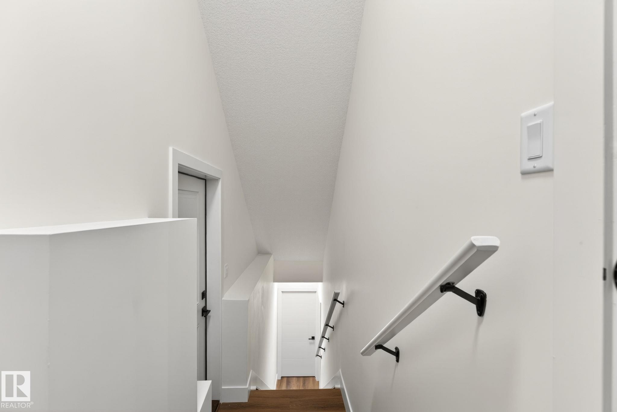 Staircase featuring wood-finish flooring, white walls, and a contemporary white handrail with black brackets - 5308 103A Avenue, Edmonton, AB - Indoor Photo Showing Other Room