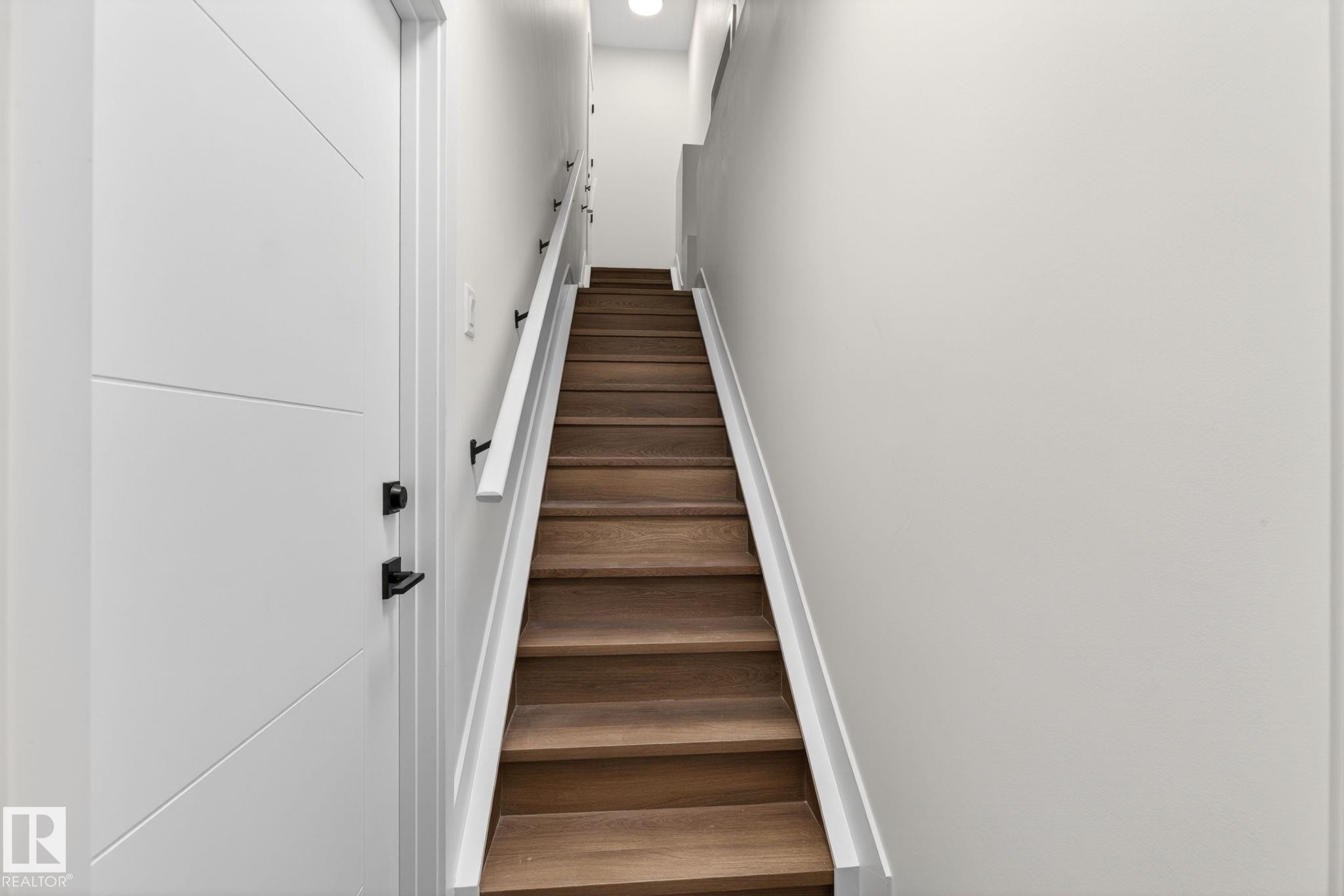 Hardwood staircase with white risers and handrail, featuring black rail supports - 5308 103A Avenue, Edmonton, AB - Indoor Photo Showing Other Room