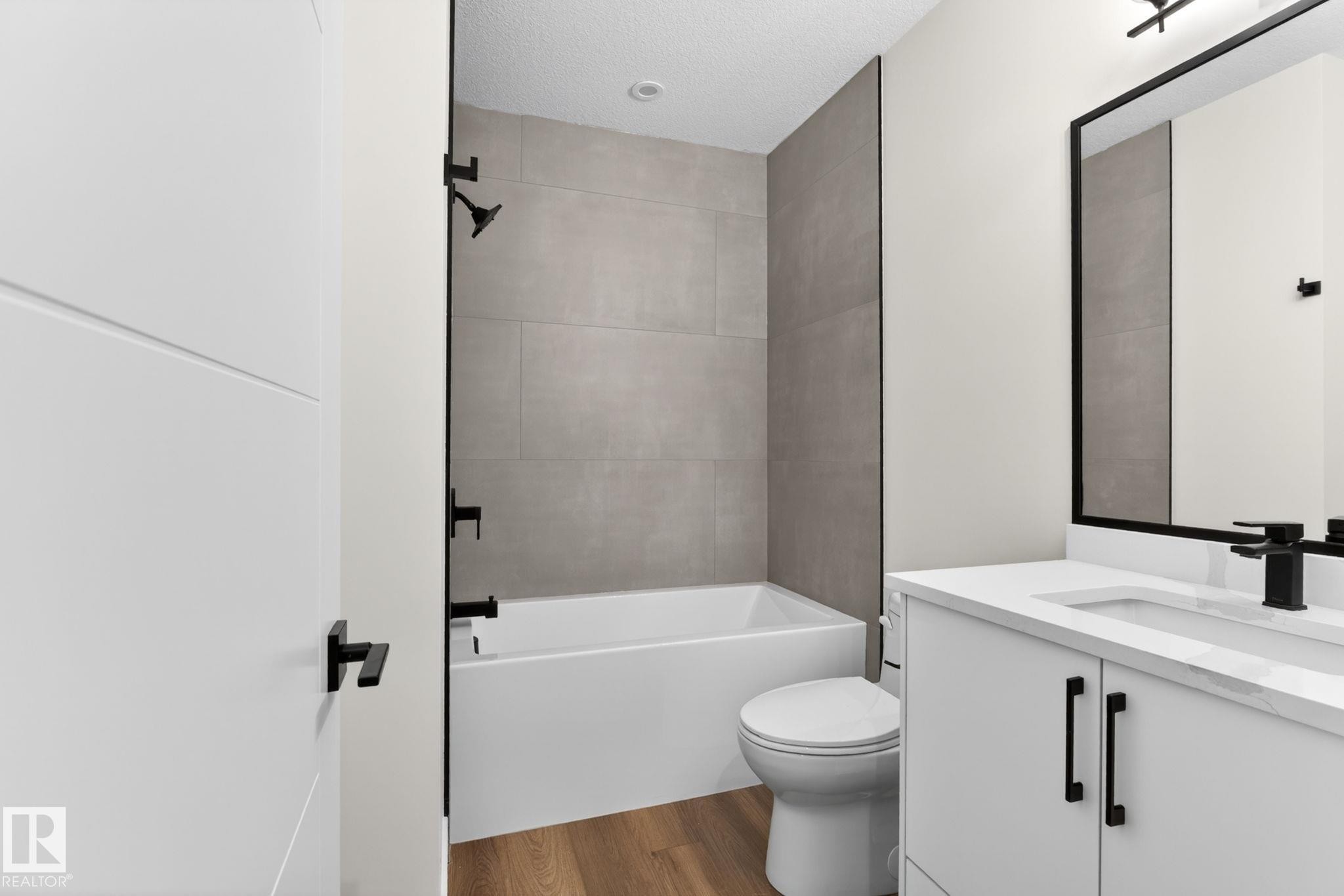 Contemporary bathroom with a white bathtub and shower featuring matte black fixtures, set against large format wall tiles - 5308 103A Avenue, Edmonton, AB - Indoor Photo Showing Bathroom