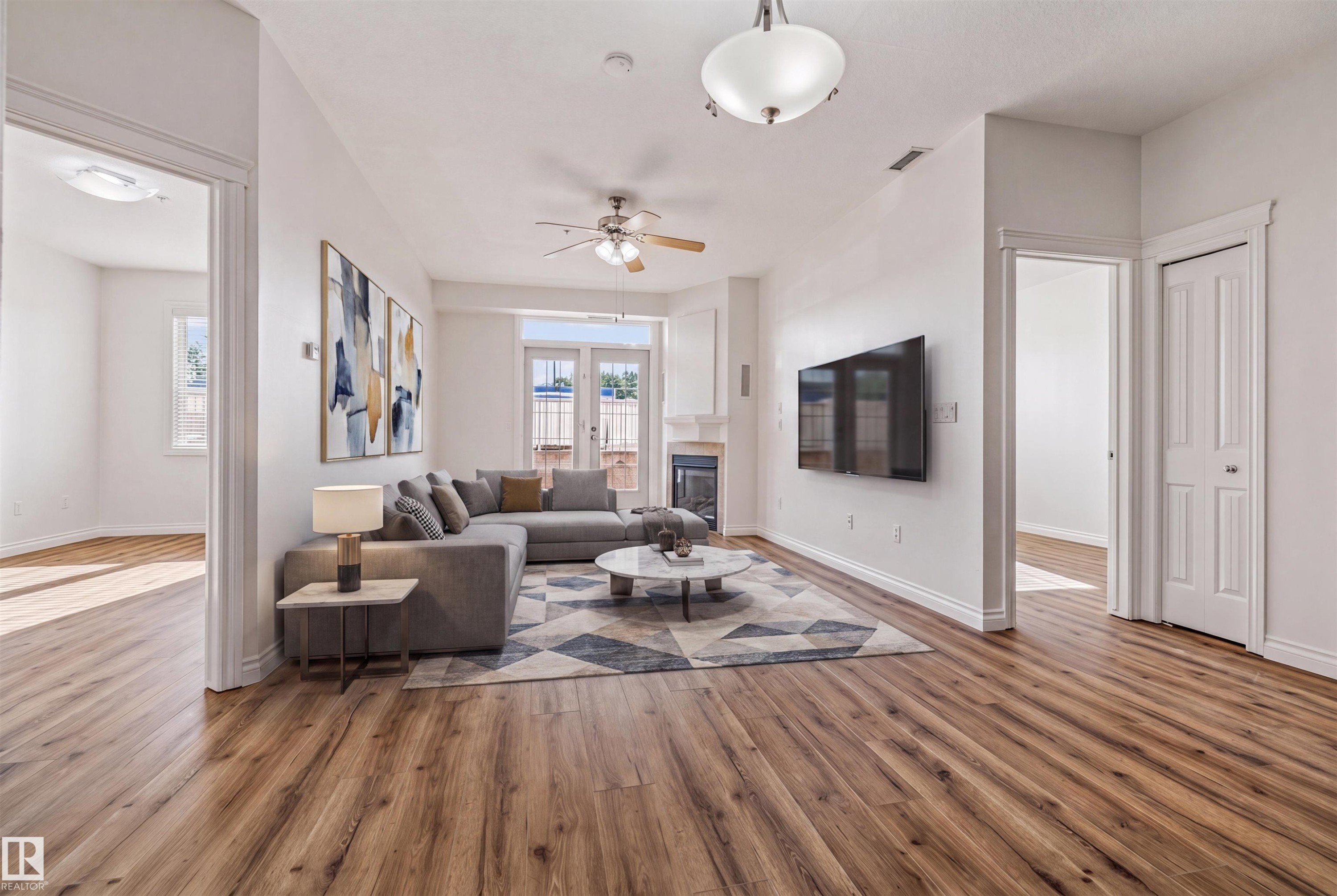 Spacious living area featuring wood-finish flooring, a fireplace with a mantel, and French doors - #110 5211 50 St, Stony Plain, AB - Indoor Photo Showing Living Room