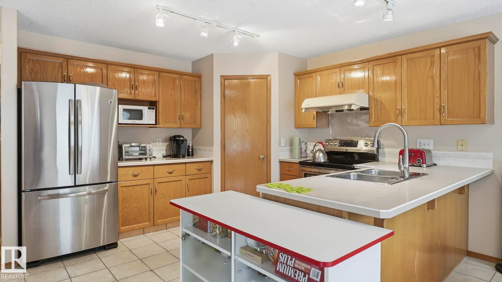 Kitchen featuring wood cabinetry, stainless steel appliances, a double basin sink, and track lighting - 125 Dechene Road Nw, Edmonton, AB - Indoor Photo Showing Kitchen With Double Sink
