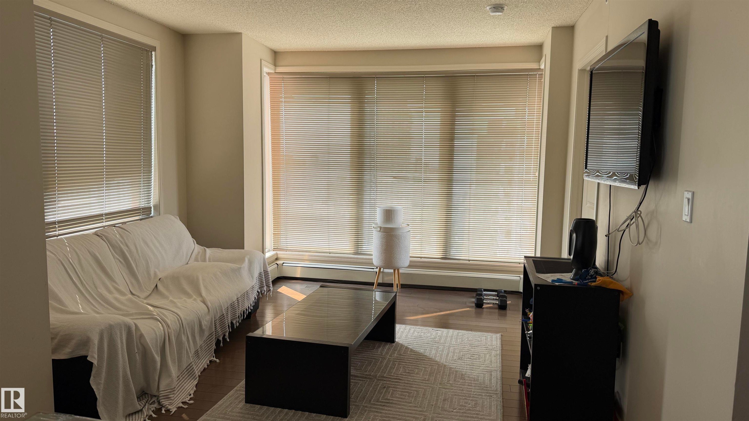Living space featuring wood-finish flooring, light neutral wall tones, and multiple large windows with horizontal blinds - #2401 10180 104 St Nw, Edmonton, AB - Indoor