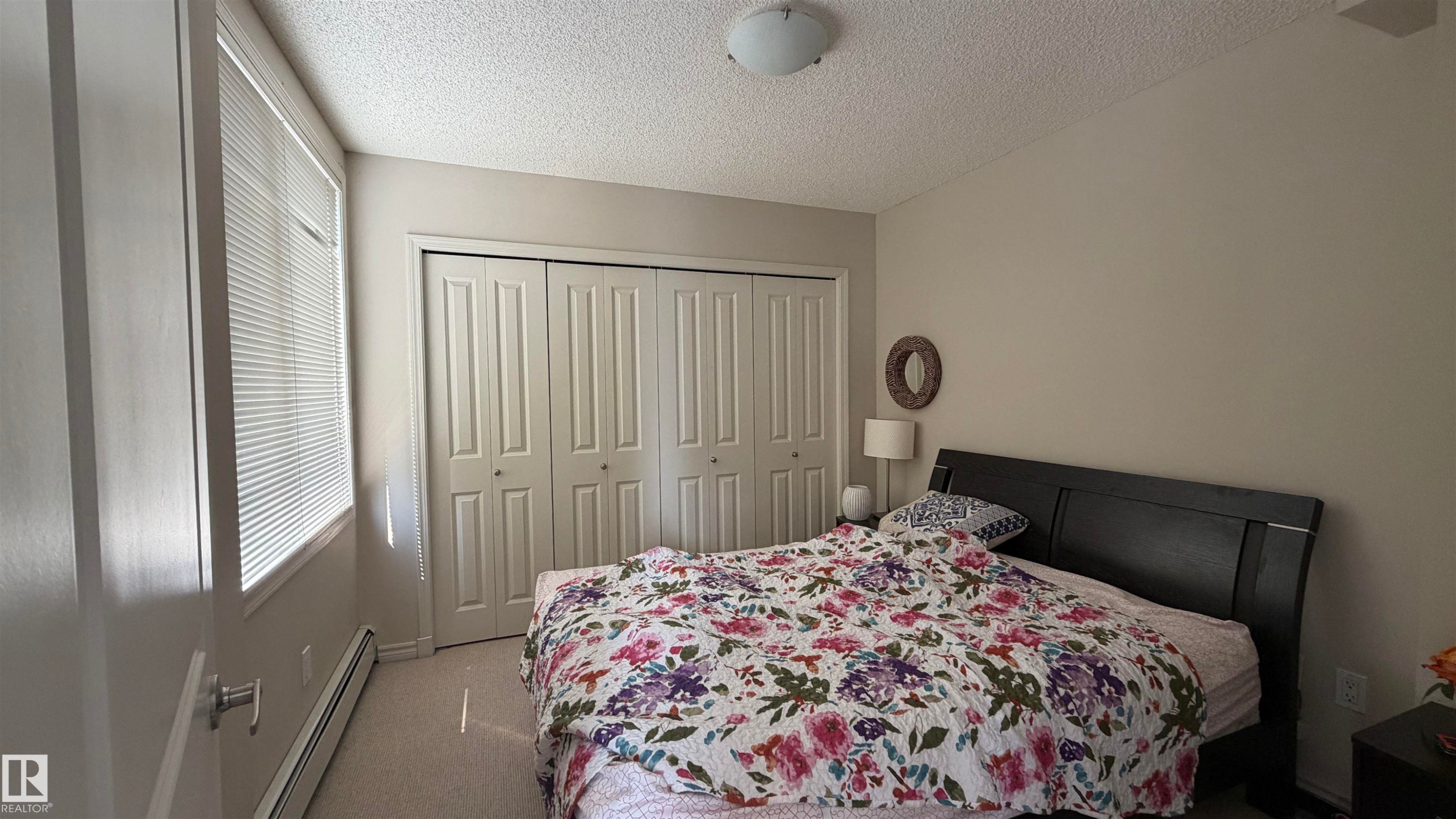 Bedroom featuring a neutral color palette, twin windows with blinds, bi-fold closet doors, and carpet flooring - #2401 10180 104 St Nw, Edmonton, AB - Indoor Photo Showing Bedroom