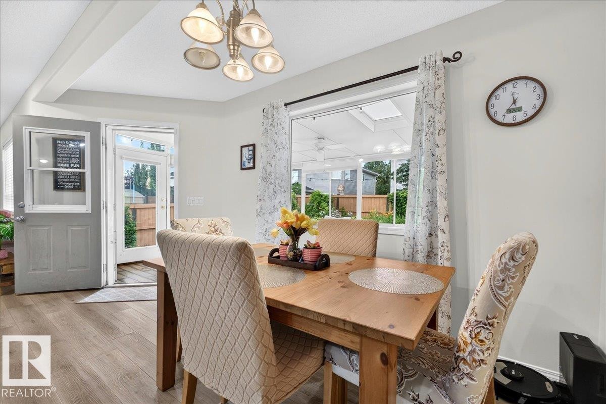 Dining area featuring wood-finish flooring, a contemporary chandelier, and a large window overlooking a sunroom - 6 Norfolk Close, St. Albert, AB - Indoor Photo Showing Dining Room
