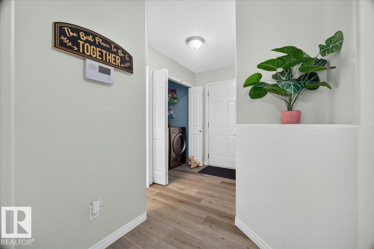 Laundry area featuring a front-loading washing machine, light wood-finish flooring, and a white paneled door - 6 Norfolk Close, St. Albert, AB - Indoor Photo Showing Other Room