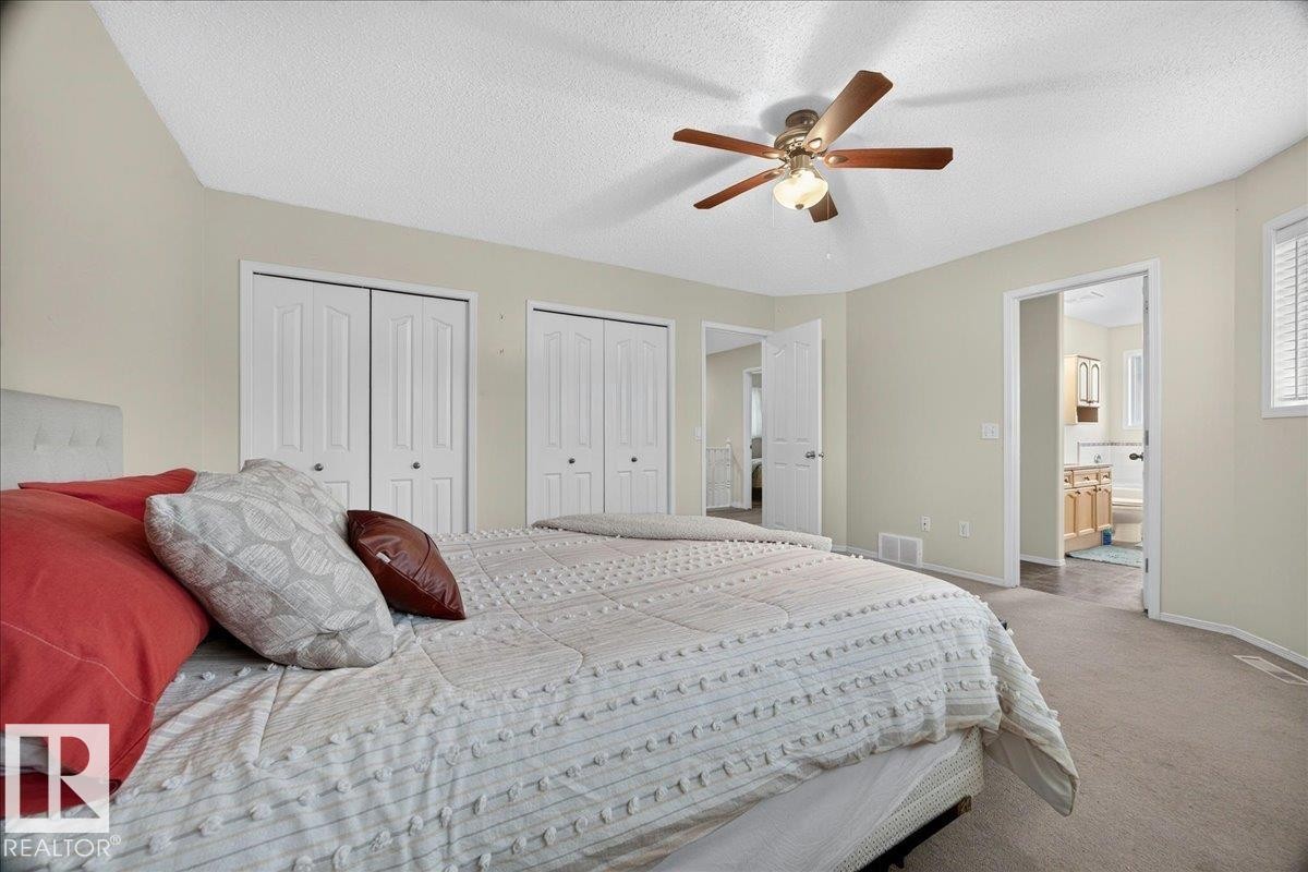 Carpeted room featuring a ceiling fan with light fixture, multiple bi-fold closet doors, and access to an adjoining bathroom - 6 Norfolk Close, St. Albert, AB - Indoor Photo Showing Bedroom