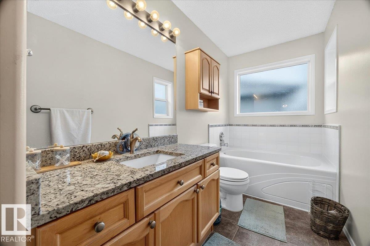 Bathroom featuring a wood-finish vanity with a granite countertop, undermount sink, and full-width mirror - 6 Norfolk Close, St. Albert, AB - Indoor Photo Showing Bathroom