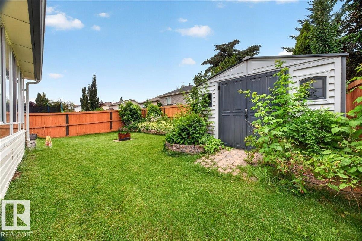 Expansive backyard featuring a manicured lawn, a grey storage shed with double doors and arched window details, and mature perimeter landscaping with a wood fence - 6 Norfolk Close, St. Albert, AB - Outdoor