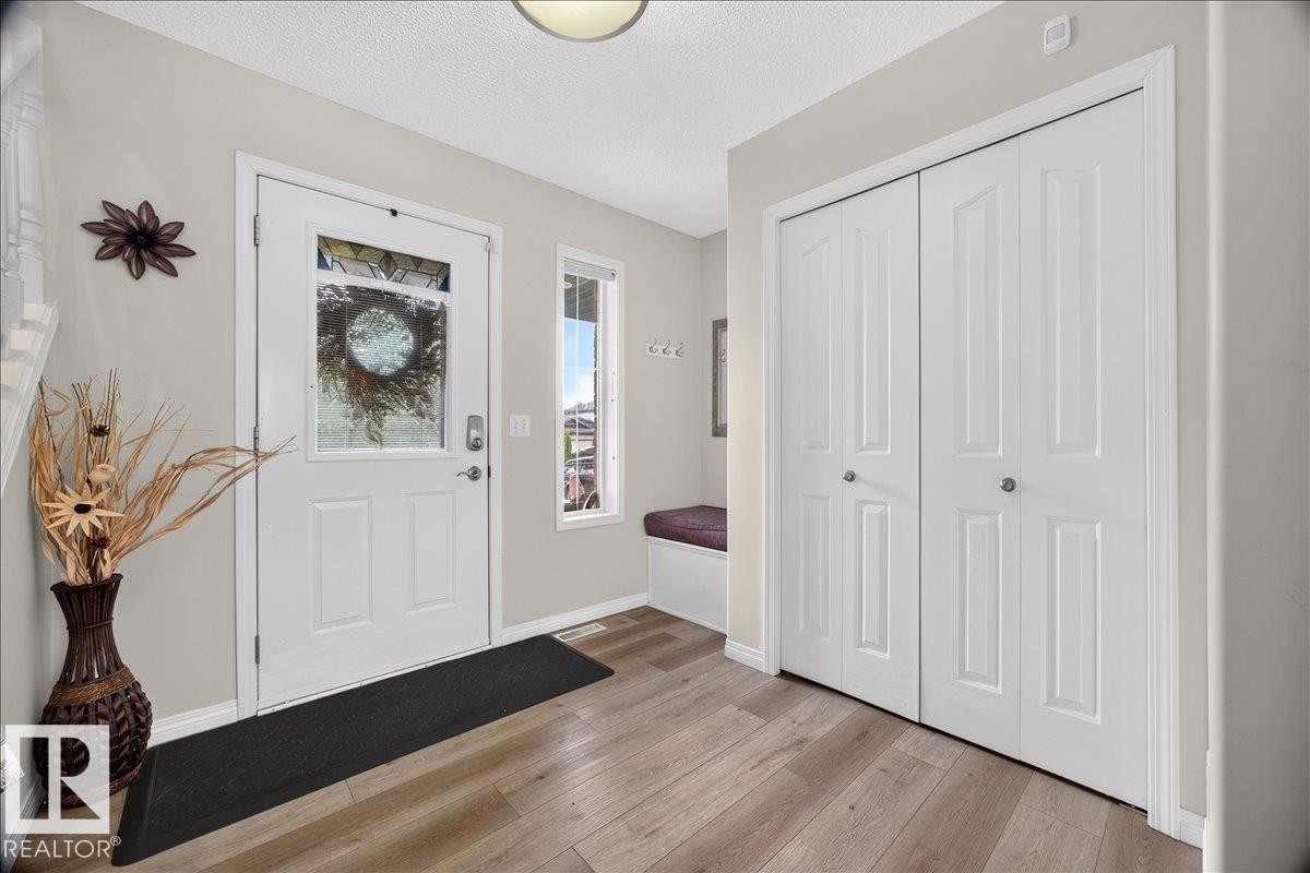 Entryway featuring wood-finish flooring, a white paneled entry door with decorative glass inlay, and a built-in bench with upholstered seating - 6 Norfolk Close, St. Albert, AB - Indoor Photo Showing Other Room