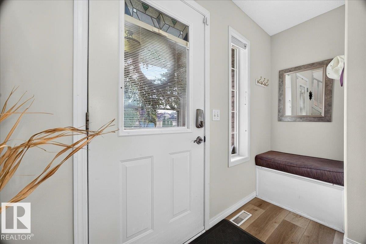 Entryway featuring a white paneled door with decorative glass, wood-finish flooring, a built-in bench with cushion, and a vertical window - 6 Norfolk Close, St. Albert, AB - Indoor Photo Showing Other Room
