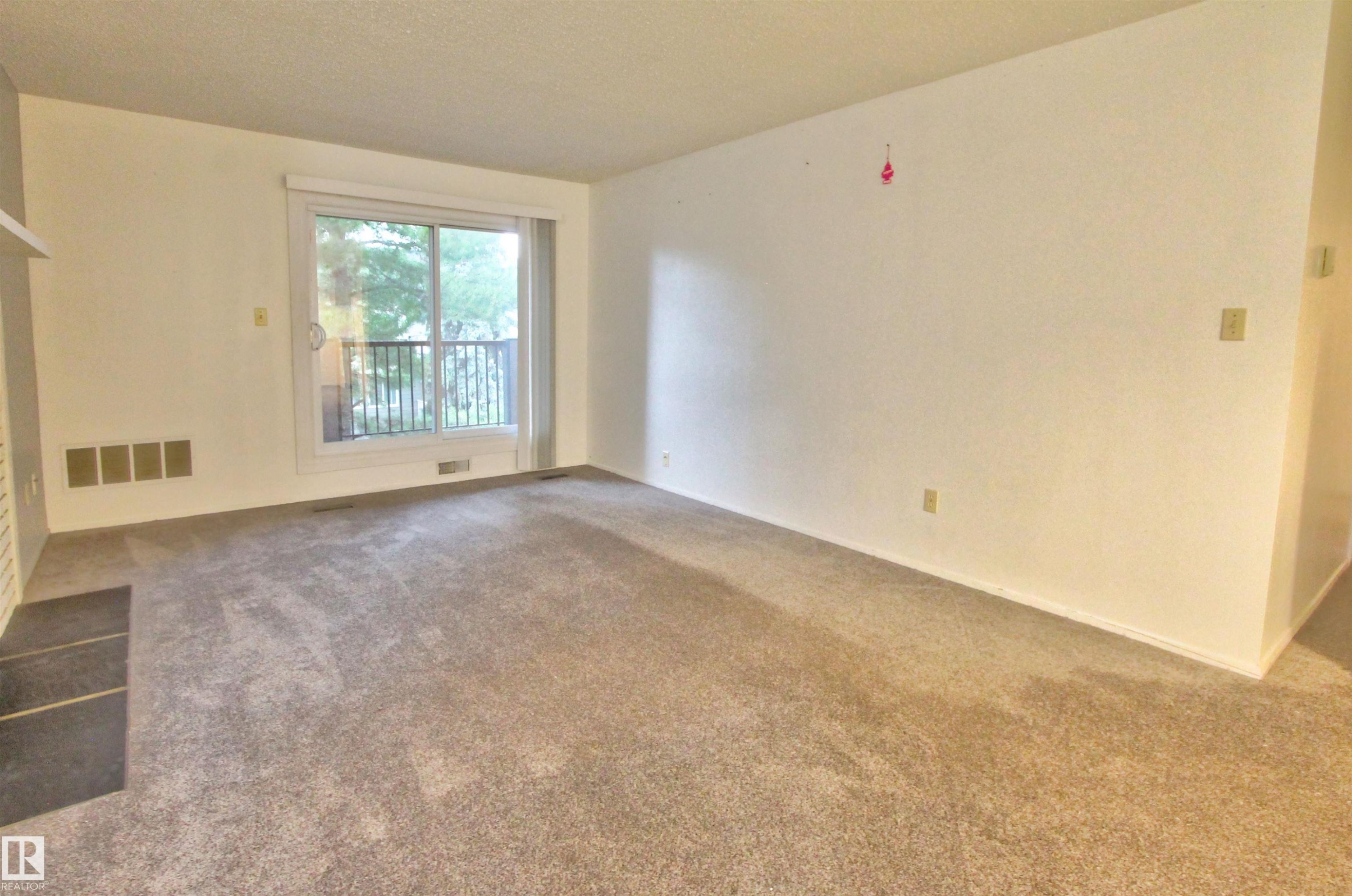 Spacious carpeted living area with a sliding glass door providing outdoor access - #302 47 Akins Dr, St. Albert, AB - Indoor Photo Showing Other Room