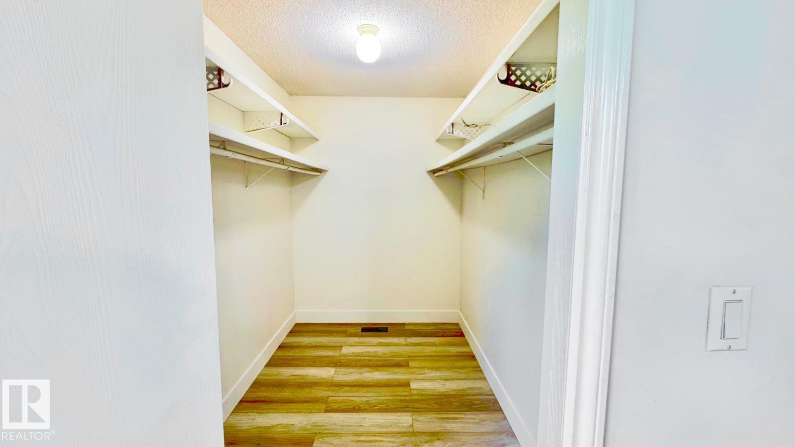 Walk-in closet featuring wood-finish flooring, white walls, built-in shelving, and hanging rods - 5144 37 Avenue Nw, Edmonton, AB - Indoor With Storage