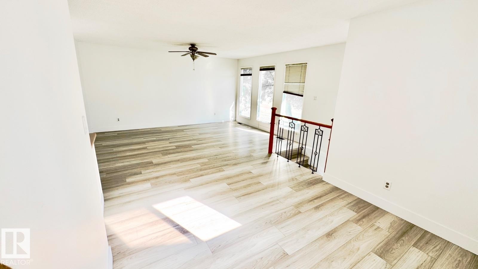 Spacious living area featuring light wood-finish flooring, a ceiling fan, and multiple windows - 5144 37 Avenue Nw, Edmonton, AB - Indoor Photo Showing Other Room