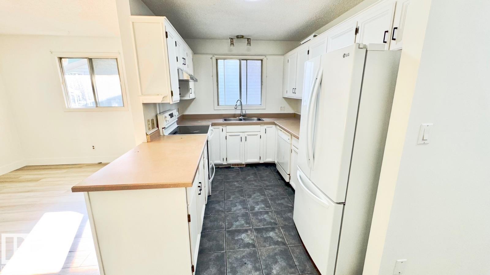 Kitchen featuring white cabinetry, light countertops, and dark tile flooring - 5144 37 Avenue Nw, Edmonton, AB - Indoor Photo Showing Kitchen With Double Sink