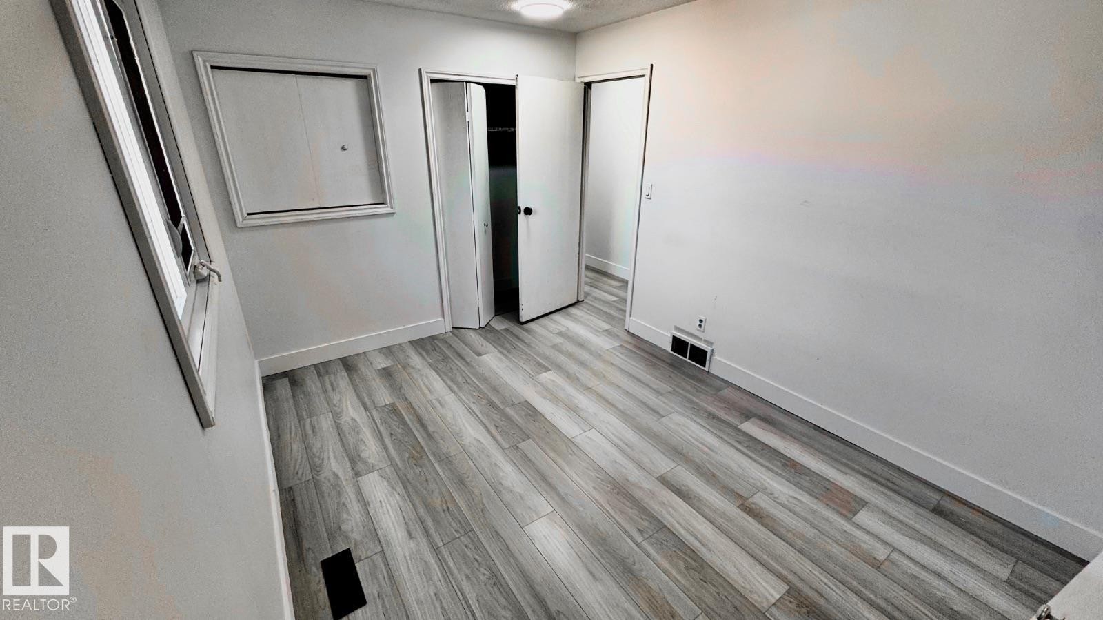 Interior room featuring wood-finish flooring, white baseboards, a window with white trim, and a built-in closet with bi-fold doors - 5144 37 Avenue Nw, Edmonton, AB - Indoor Photo Showing Other Room