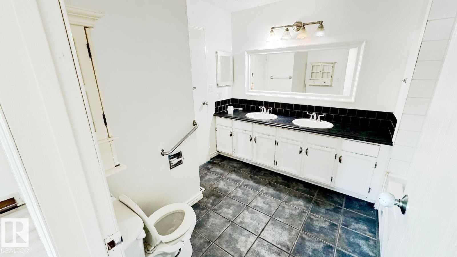 Bathroom featuring a dual vanity with white cabinetry, a dark countertop, and black tile backsplash - 5144 37 Avenue Nw, Edmonton, AB - Indoor