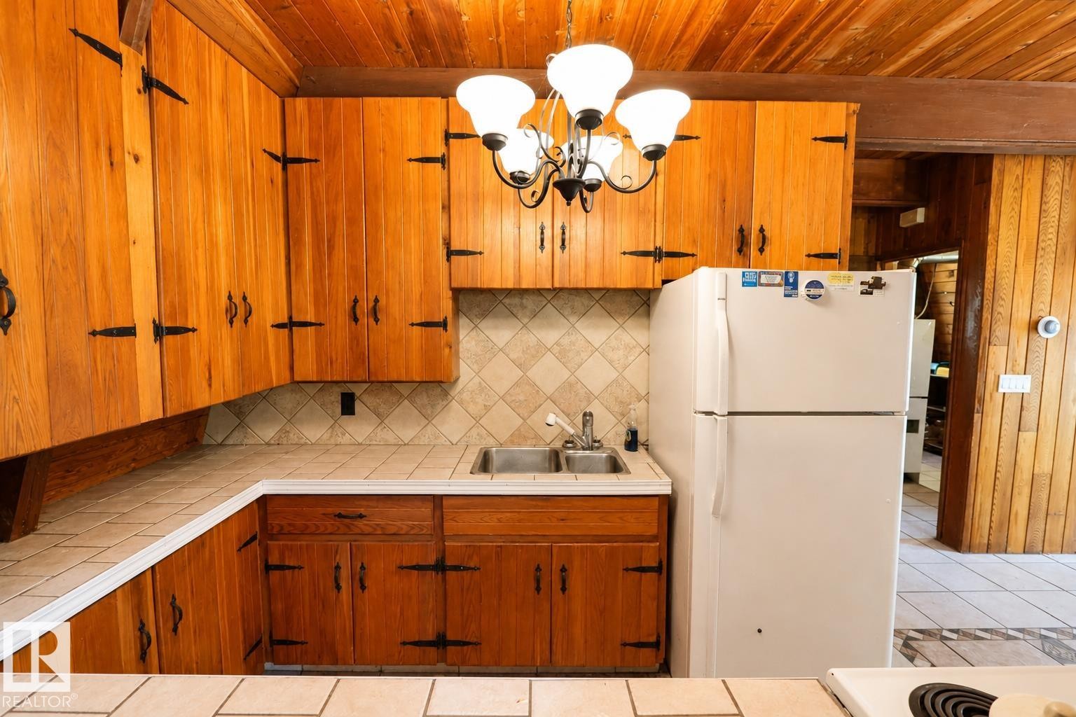 Kitchen featuring extensive wood cabinetry with decorative black hardware, a tile backsplash, and a double basin sink - 329 60417 Range Road 124, Rural St. Paul County, AB - Indoor Photo Showing Kitchen With Double Sink