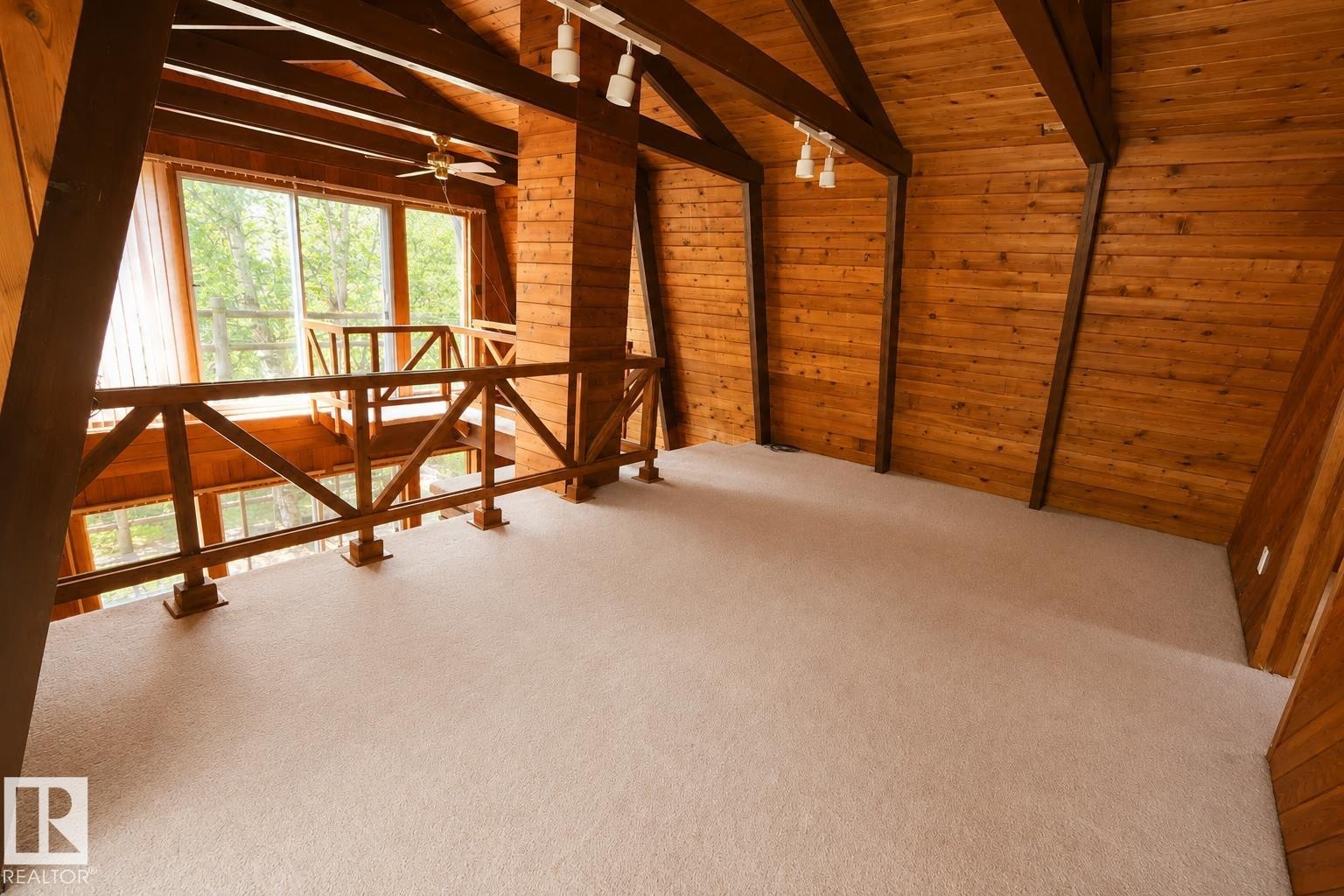 Carpeted loft area with wood-paneled walls and ceiling, exposed structural beams, track lighting, and a wood railing overlooking the lower level with large windows - 329 60417 Range Road 124, Rural St. Paul County, AB - Indoor Photo Showing Other Room