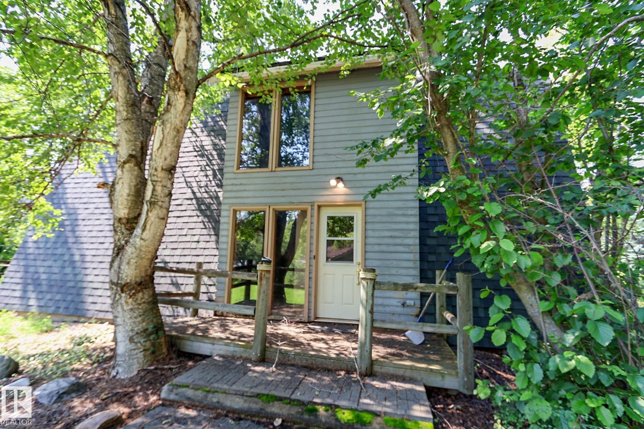Exterior featuring a light-colored entry door, an outdoor wall sconce, and a wood-finish deck with railings - 329 60417 Range Road 124, Rural St. Paul County, AB - Outdoor