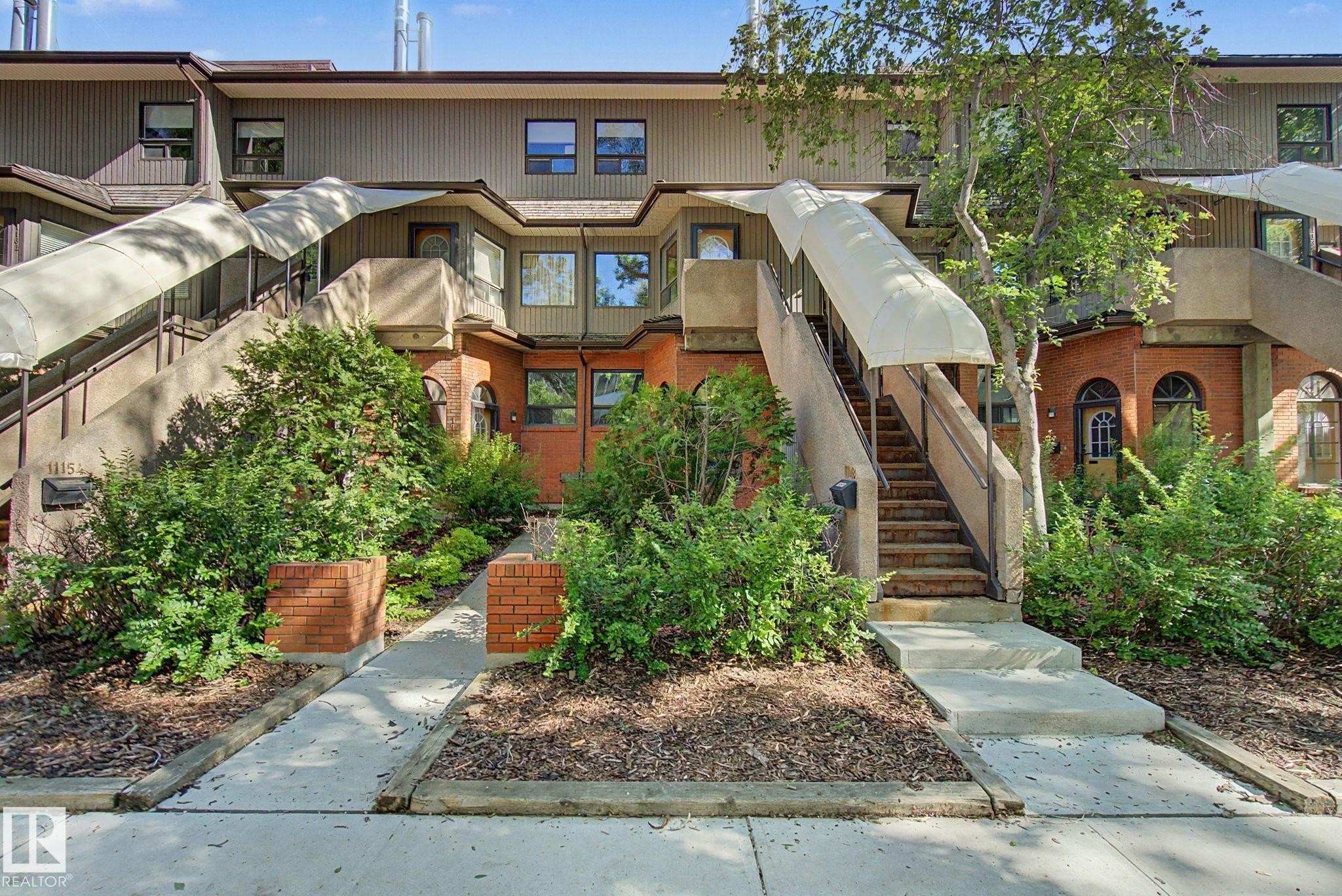 Multi-level townhouse exterior featuring brick and siding finishes, concrete stairs with metal railings, and a fabric awning - 11150 83 Avenue Nw, Edmonton, AB