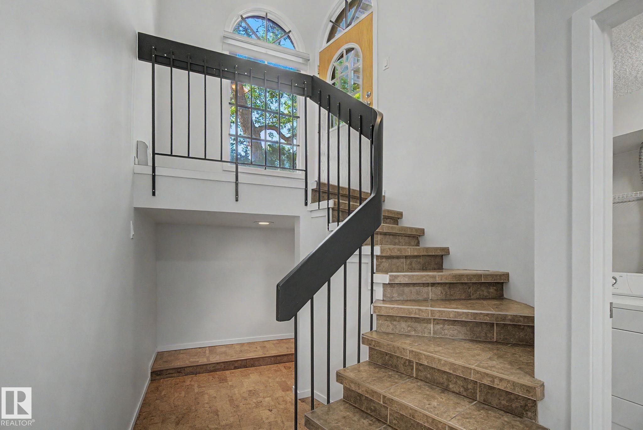 Curved staircase featuring tiled treads and a black metal railing - 11150 83 Avenue Nw, Edmonton, AB